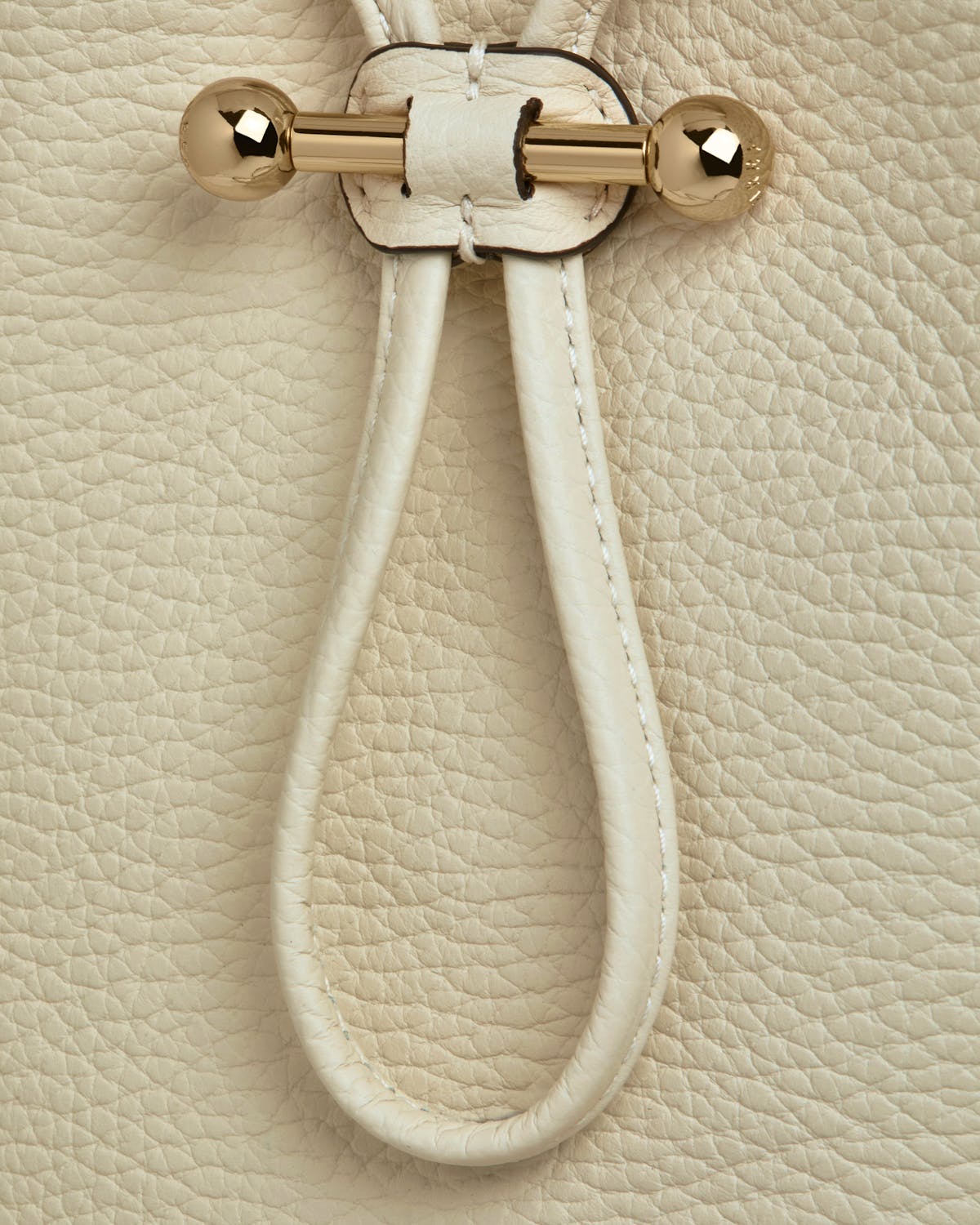 Vanilla leather pouch strap loop with gold barbell hardware and pebbled texture