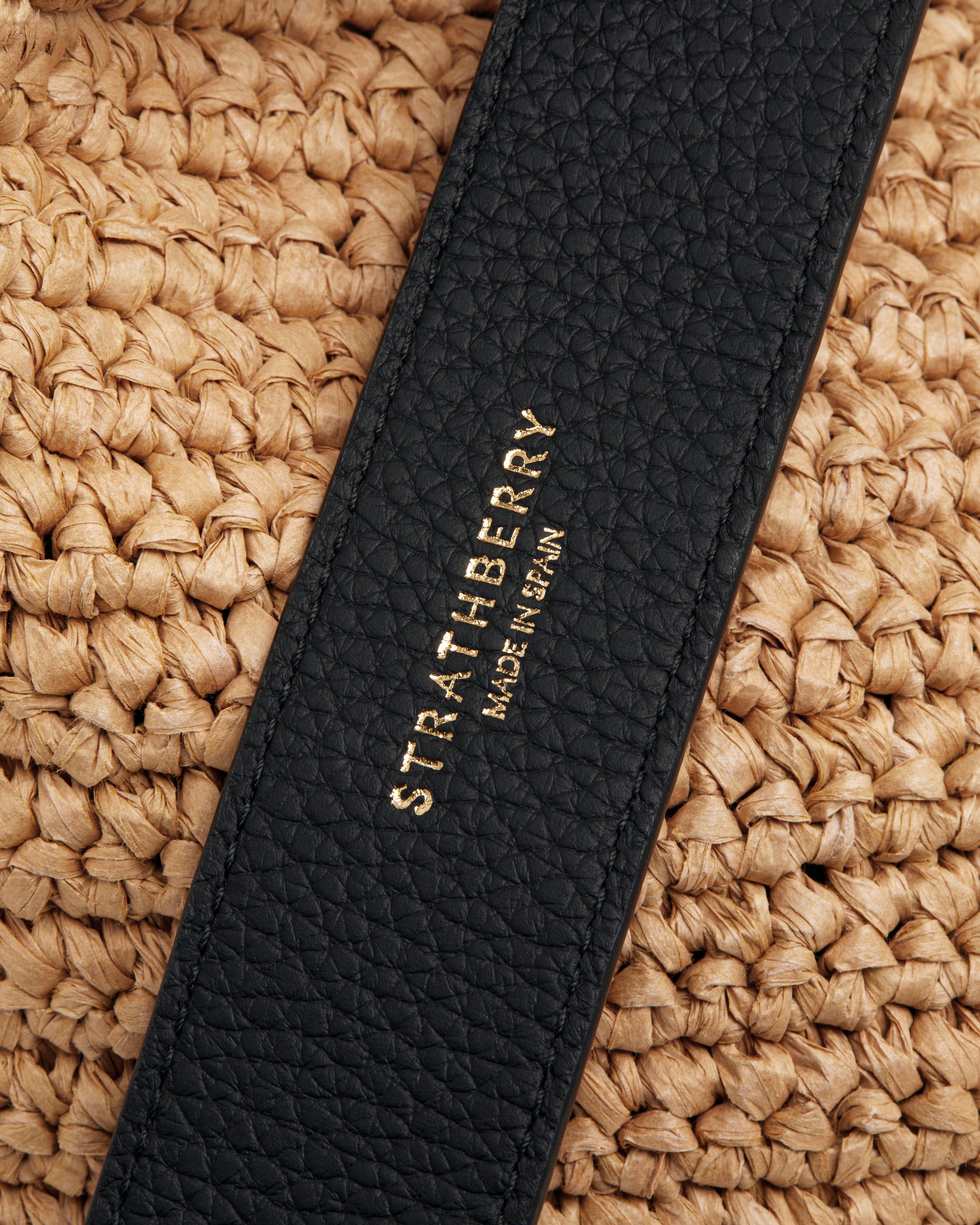 A close up of a straw bag with a black strap