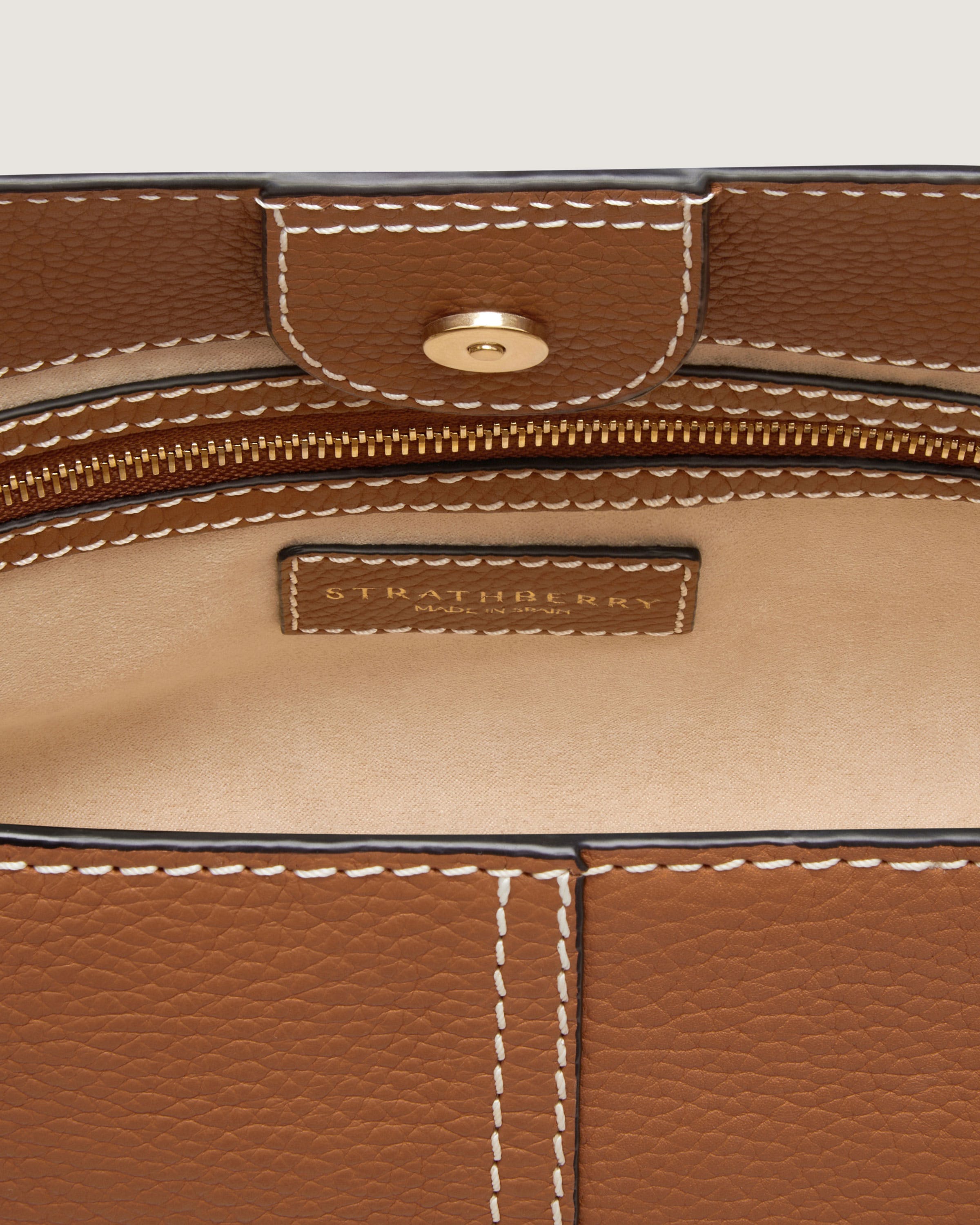 A close up of a brown purse with white stitching