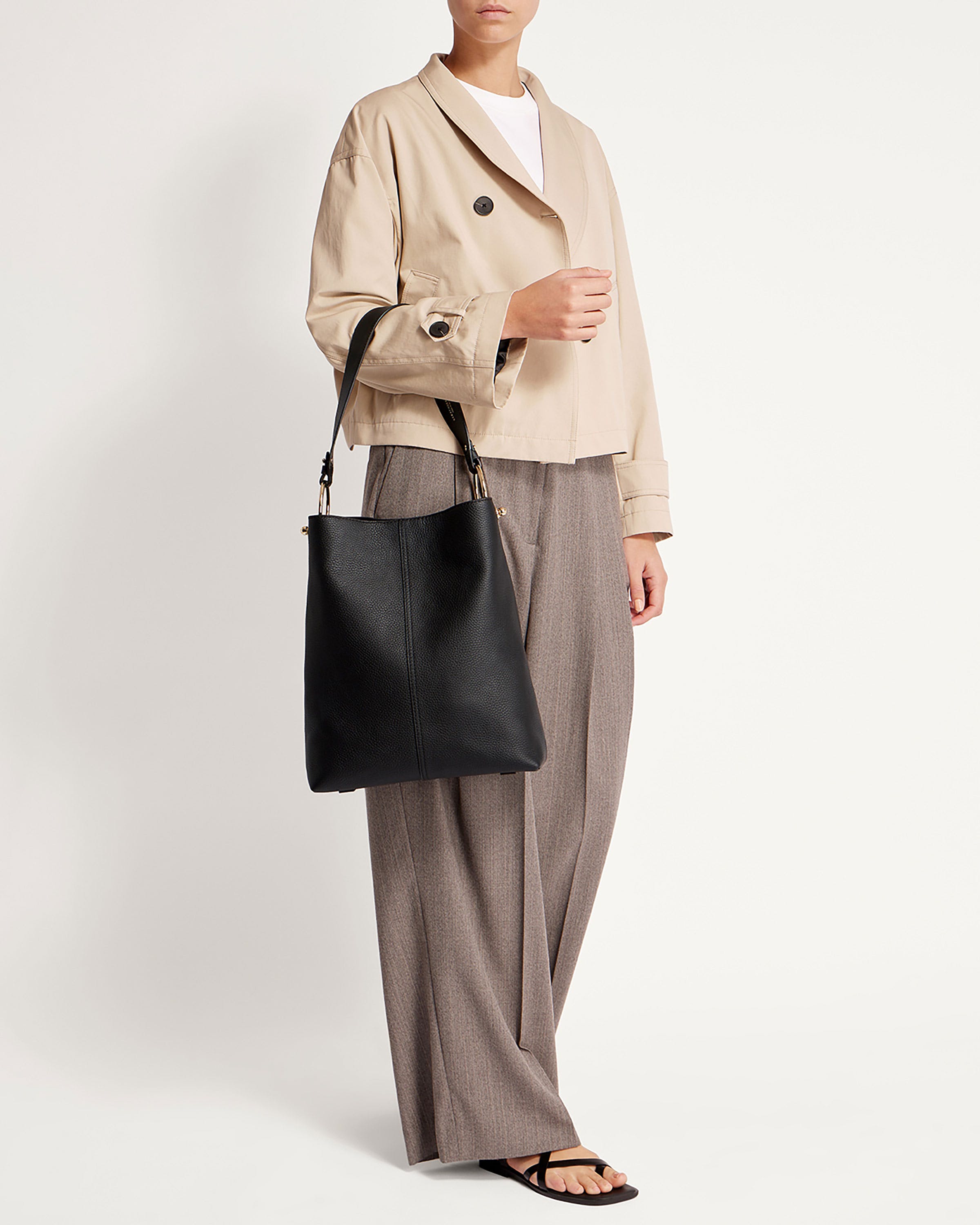 A woman is holding a black bag and a beige jacket