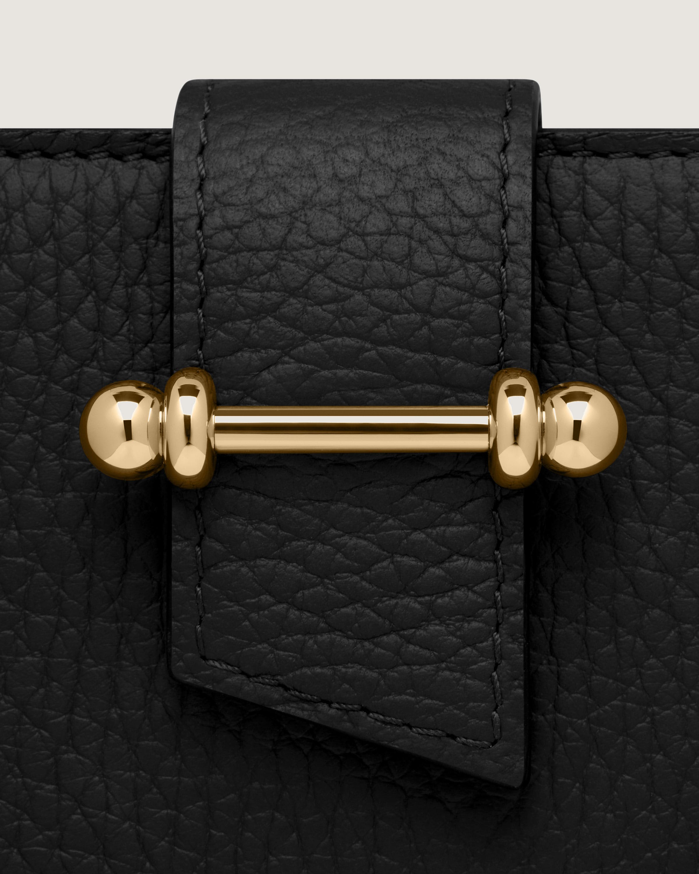 A close up of a black leather bag with a gold handle