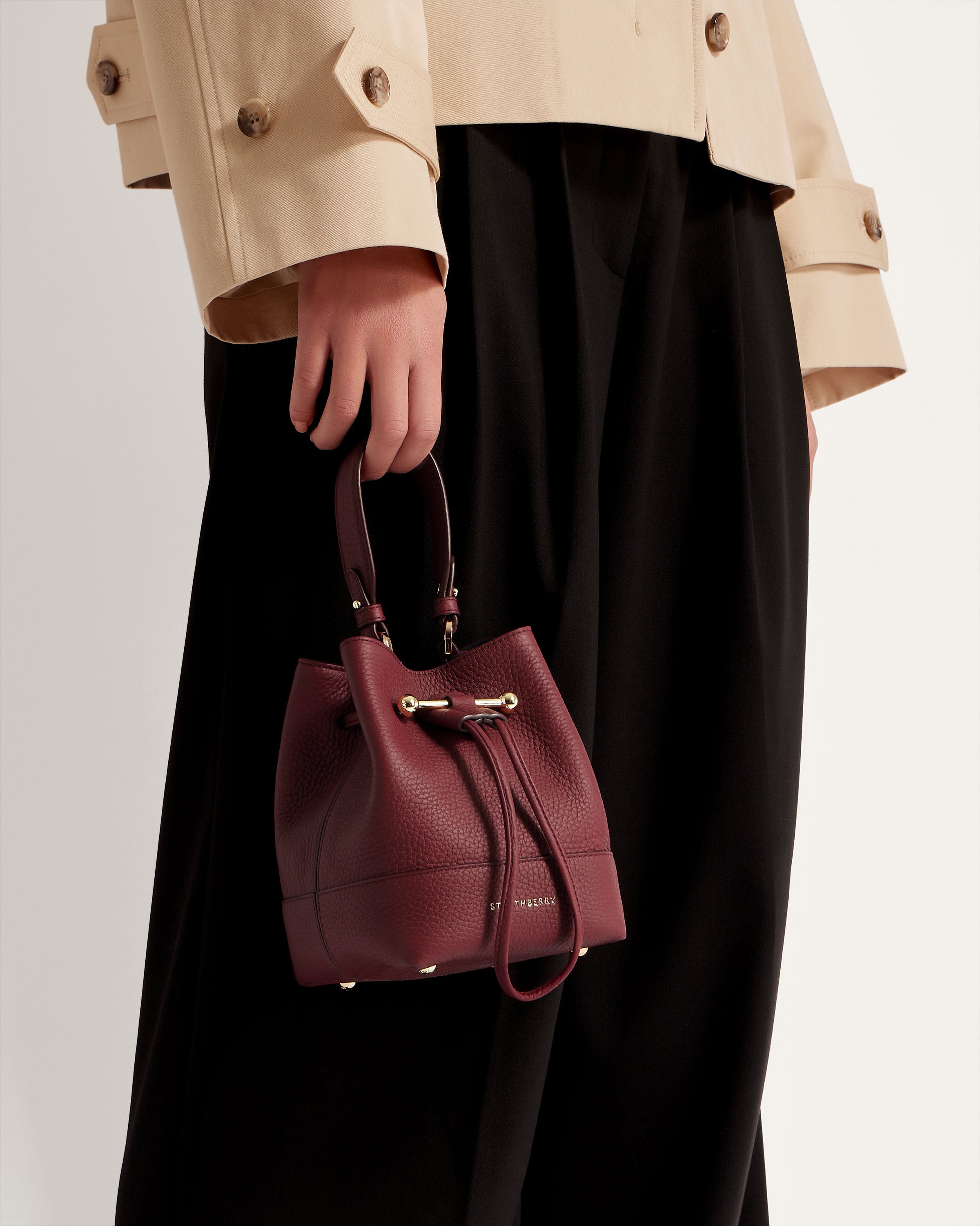 A woman in a trench coat carrying a burgundy purse