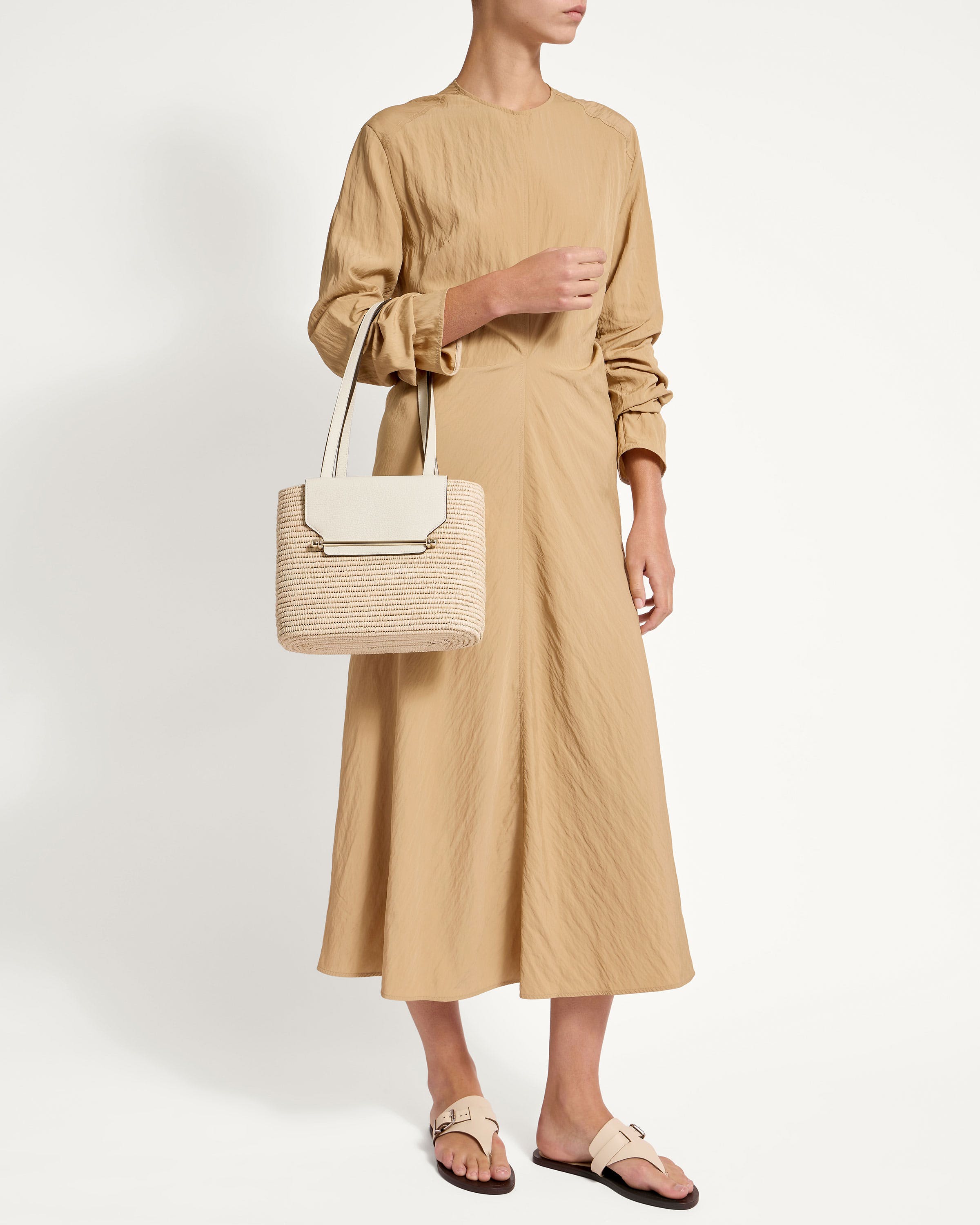 A woman in a tan dress holding a white bag