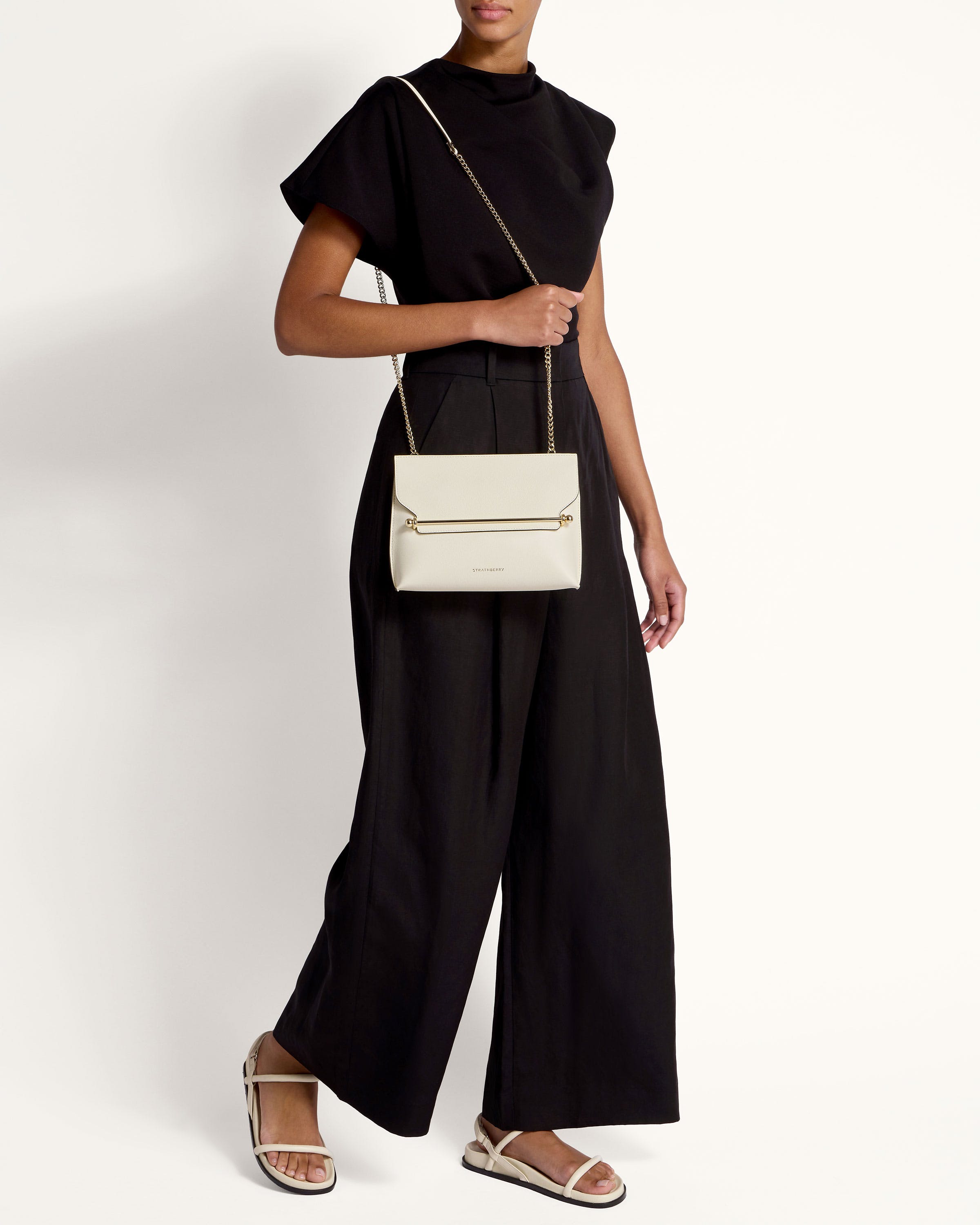 A woman in a black top and black pants holding a white purse