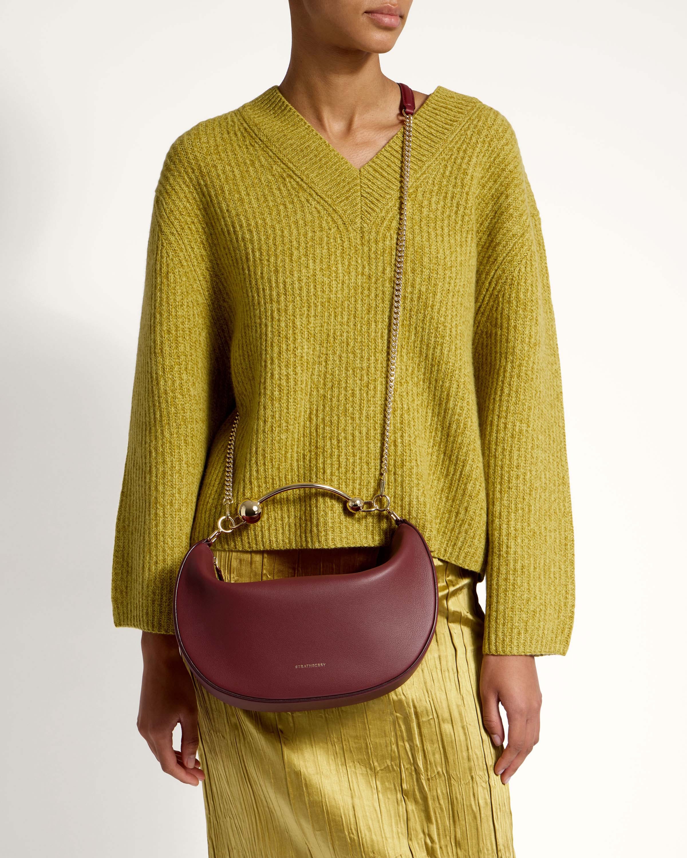 A woman in a yellow sweater holding a burgundy purse