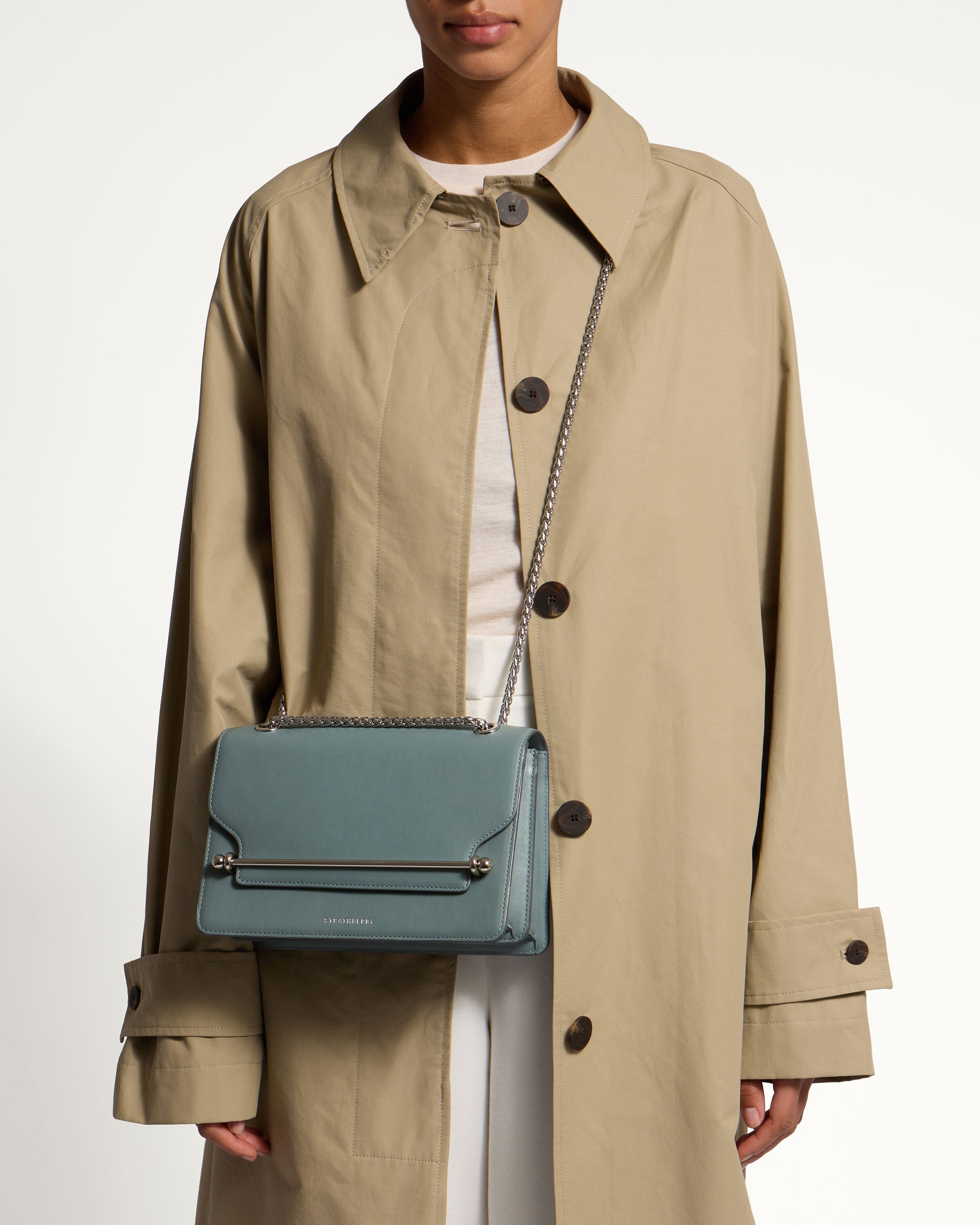 A woman in a trench coat holding a blue purse