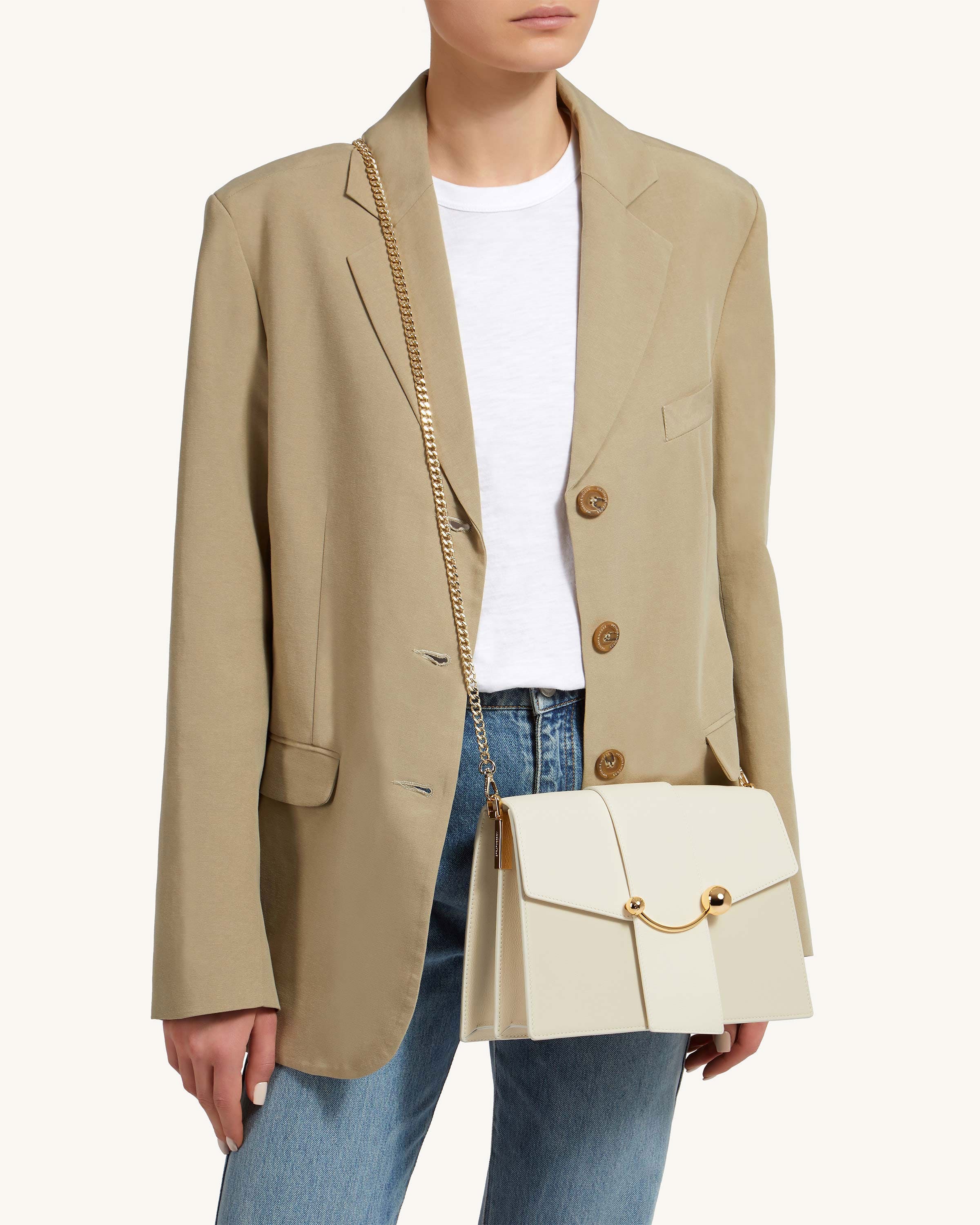 A woman wearing a tan blazer holding a white purse