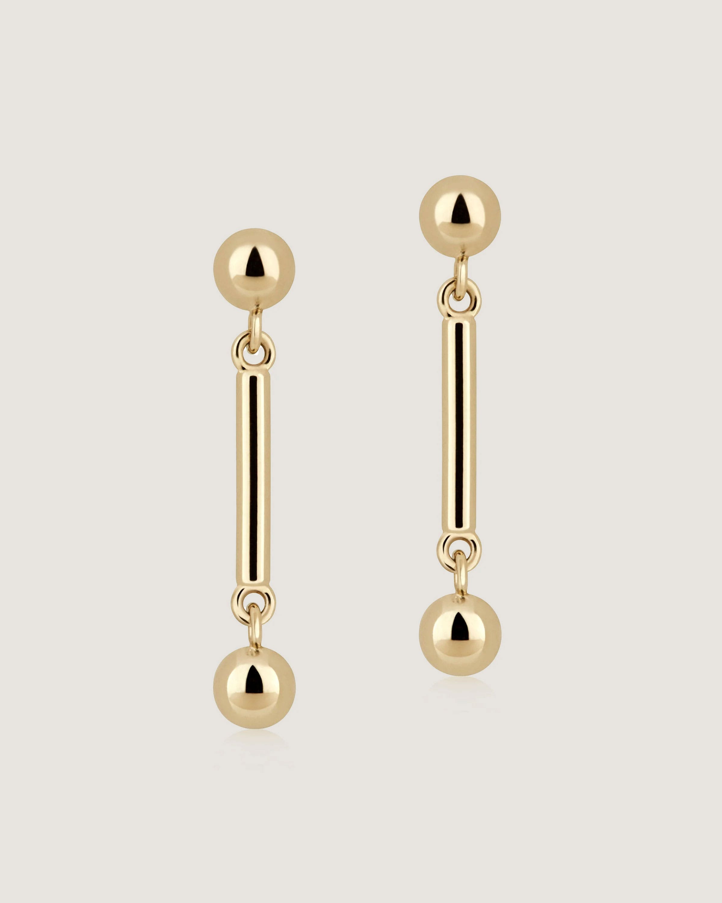 A pair of gold earrings with two balls hanging from them