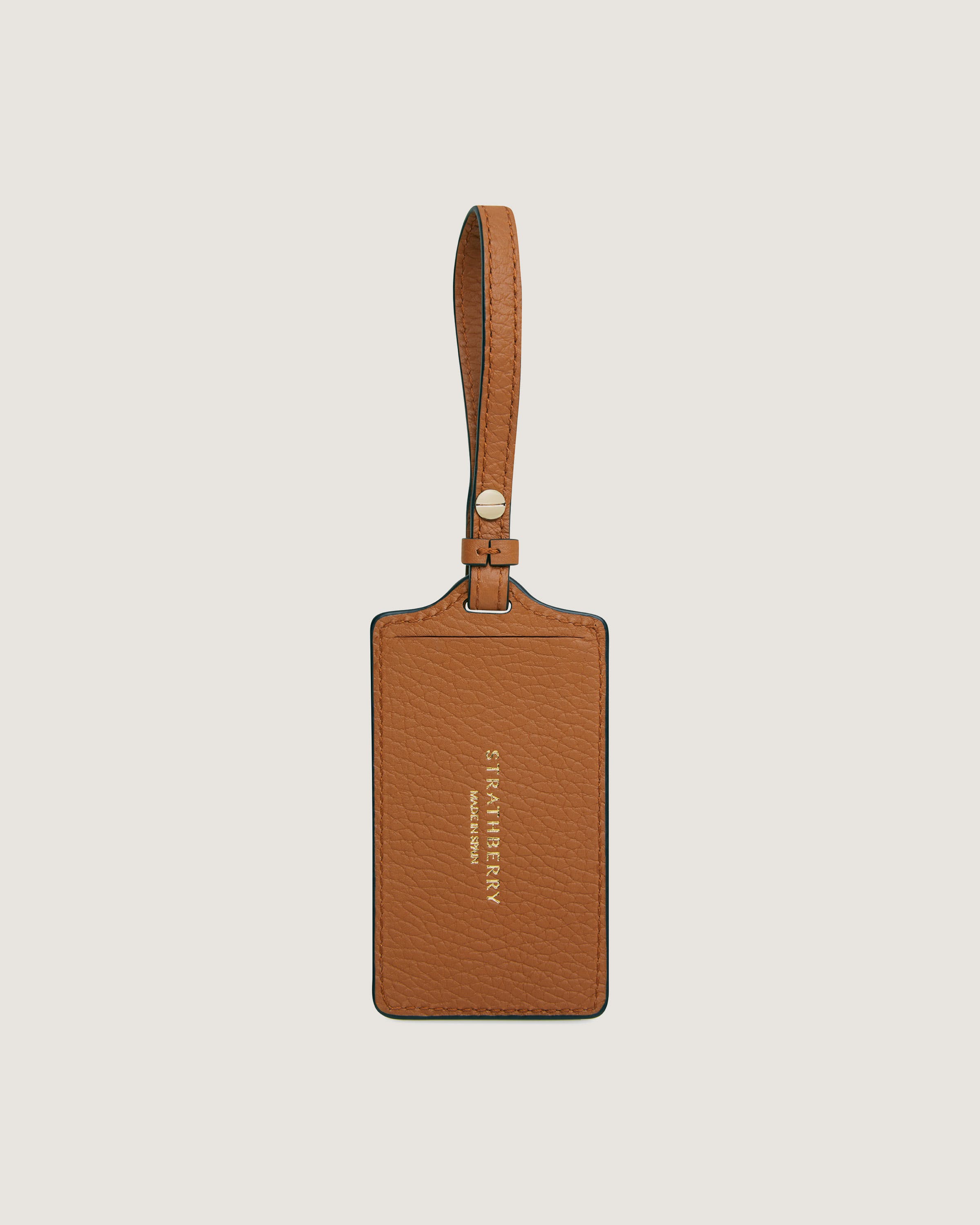 A tan leather luggage tag hanging on a white wall