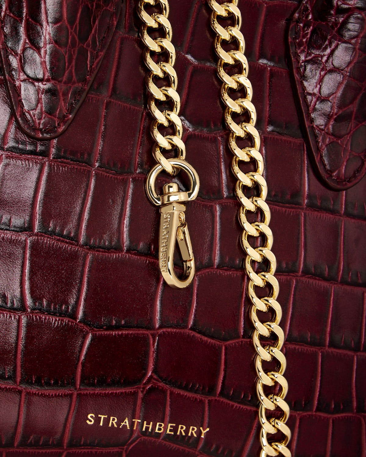 Burgundy croc-embossed leather nano tote with gold chain and Strathberry logo.
