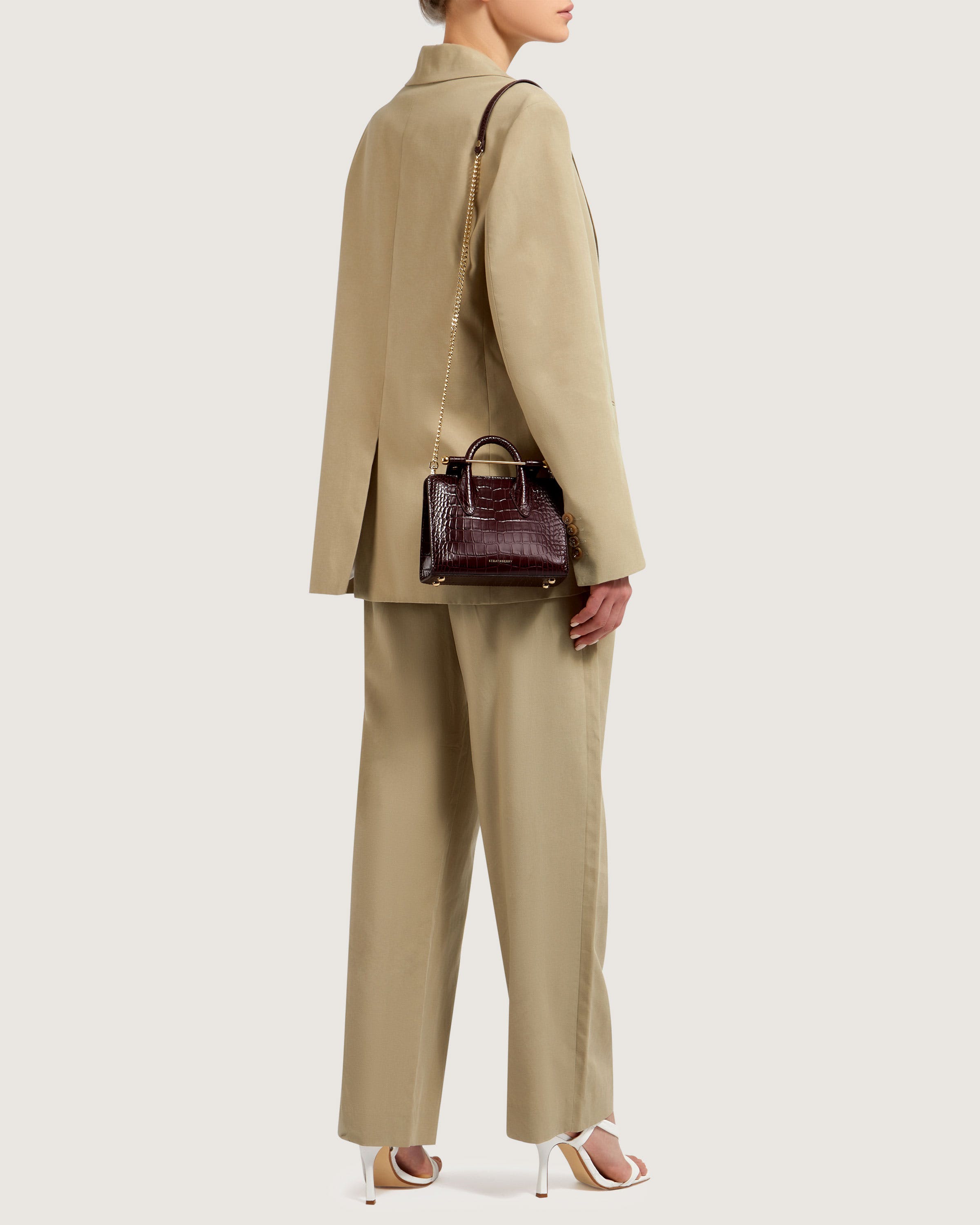 A woman in a tan suit and heels holding a brown handbag