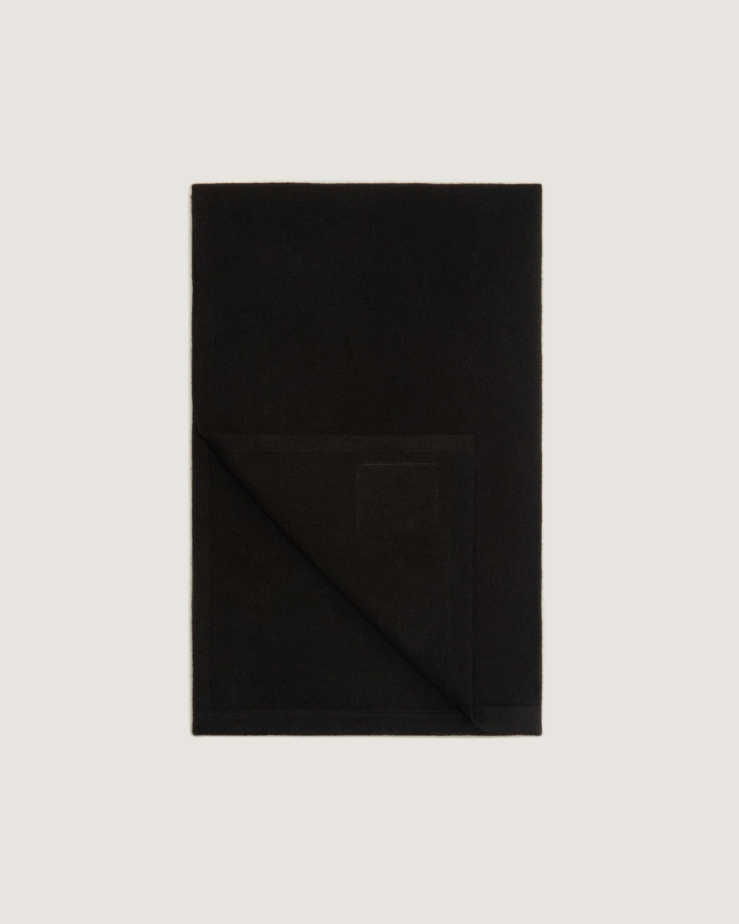 A black blanket folded on top of a white wall