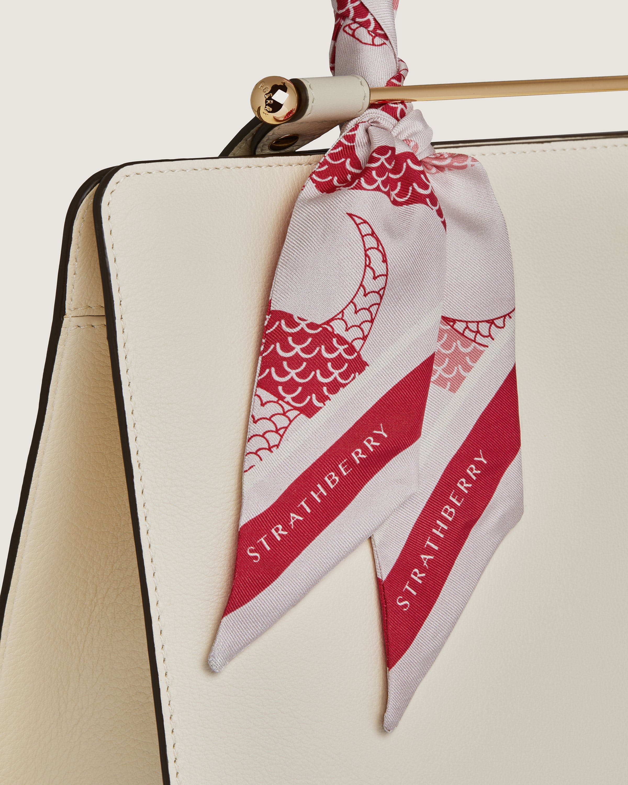 A white purse with a red and white scarf hanging from it