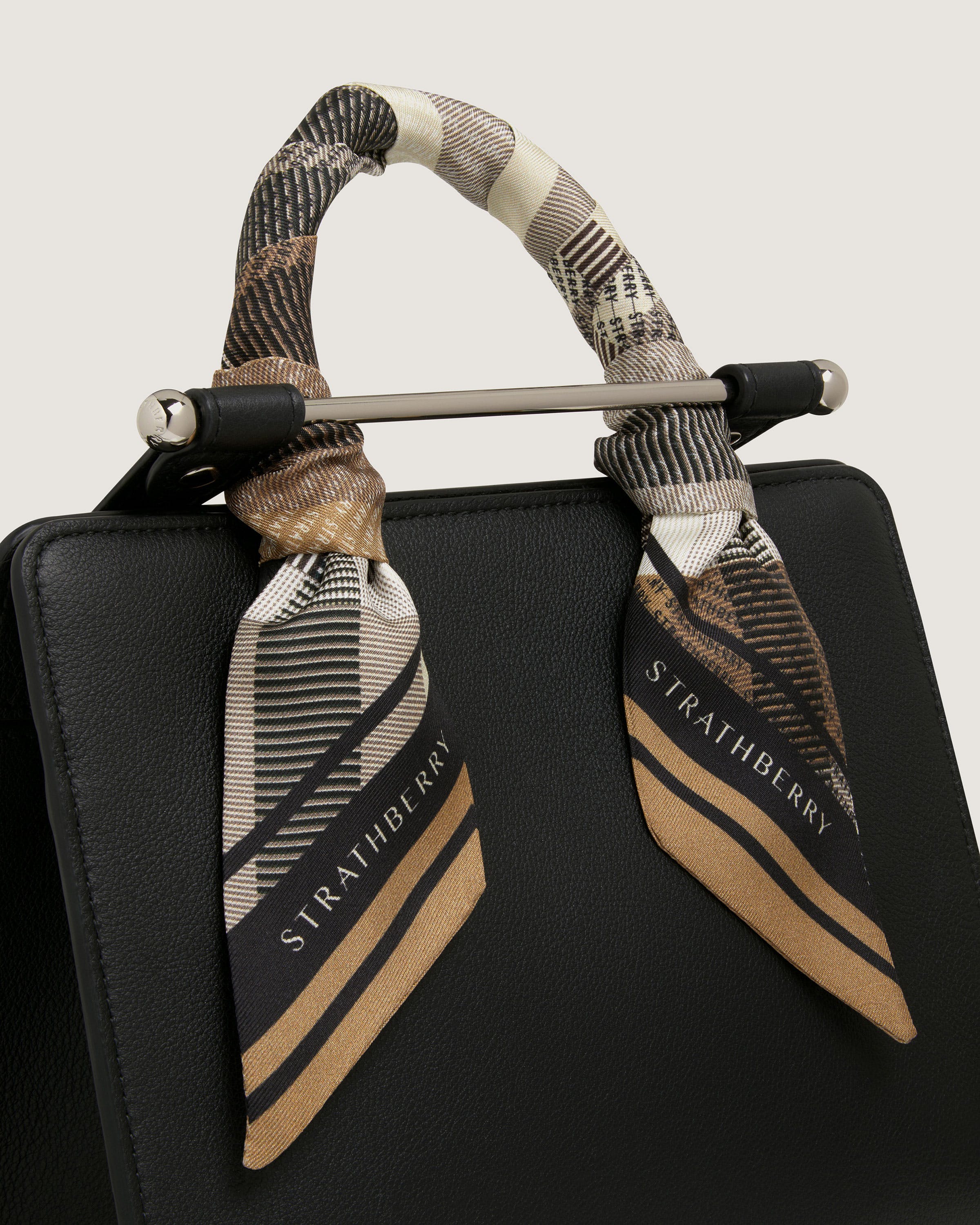 A black handbag with a brown and white scarf on it