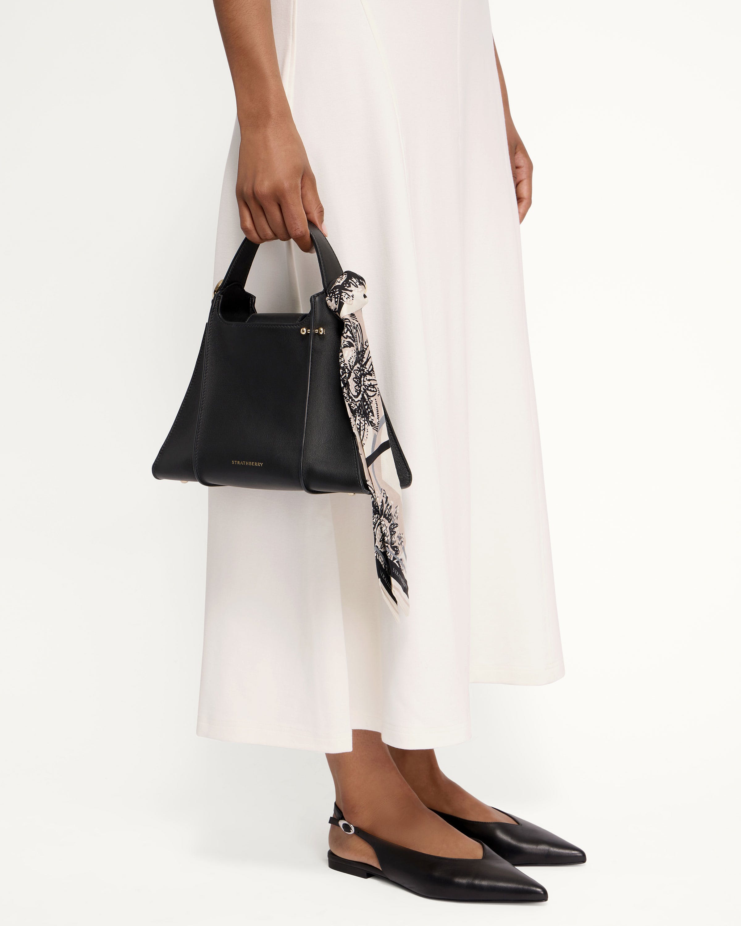 A woman in a white dress holding a black handbag