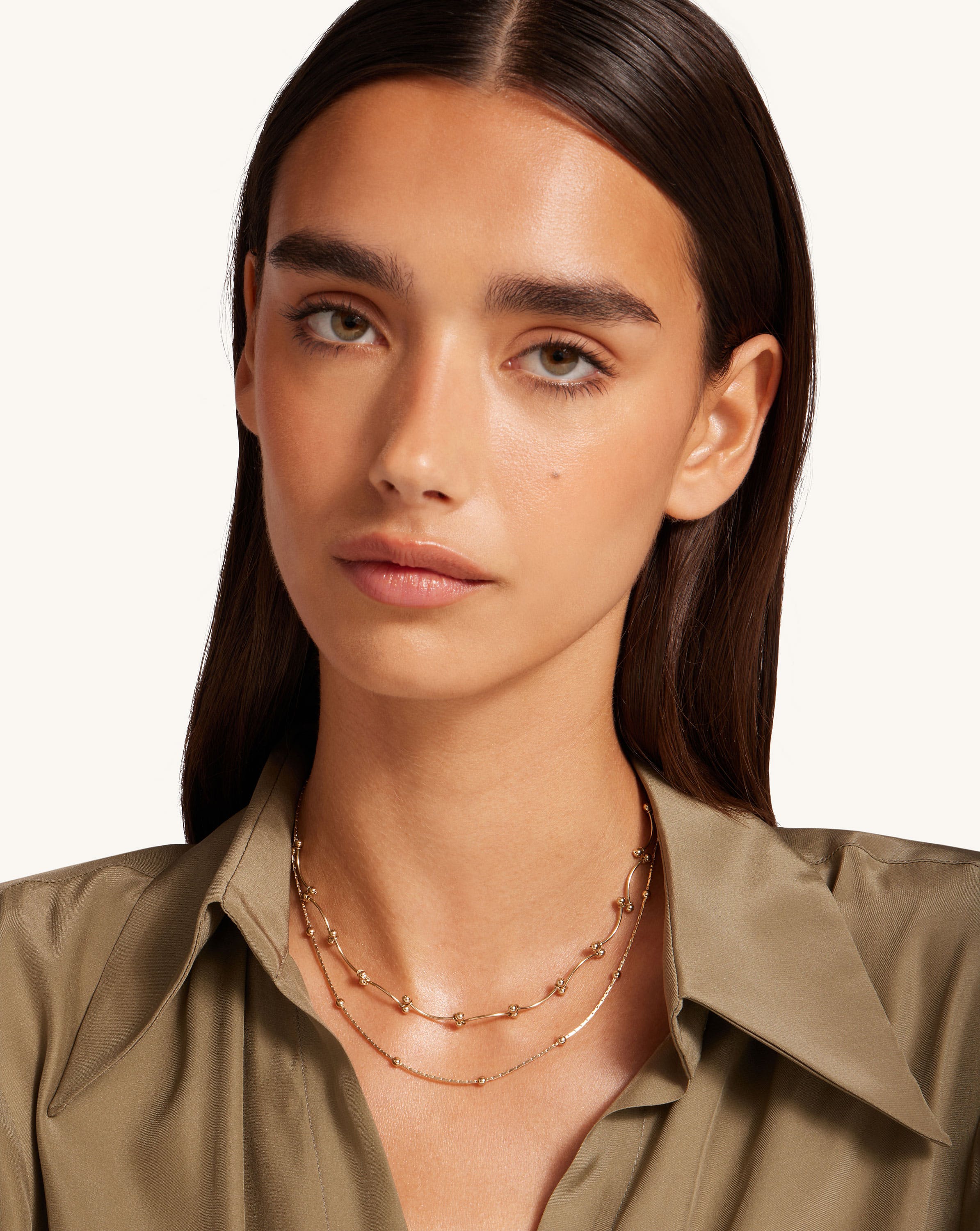 A woman wearing a tan shirt and a gold necklace