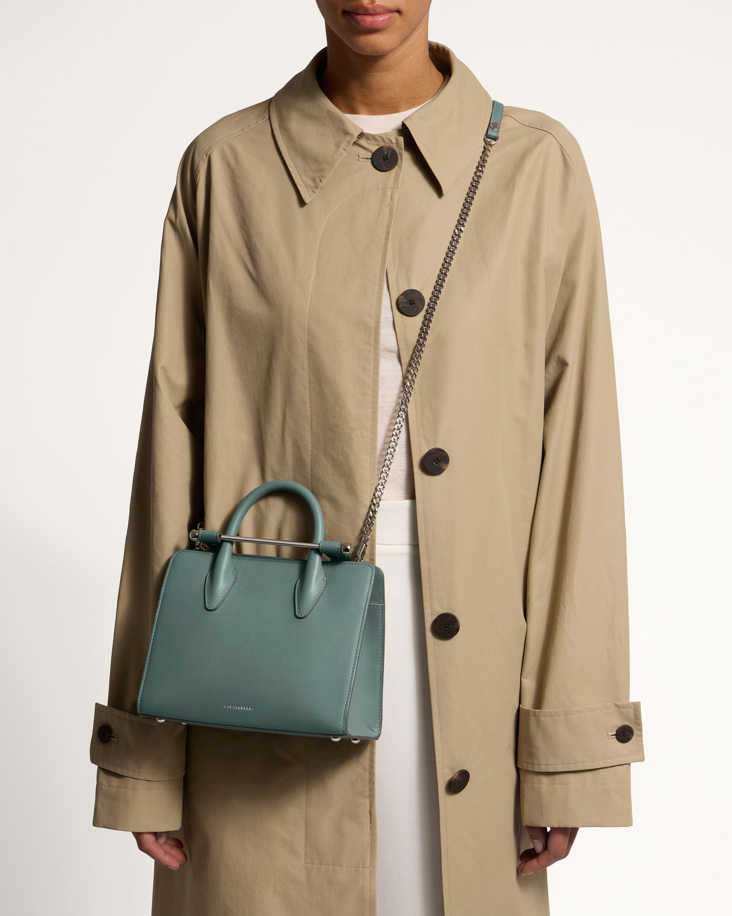 A woman in a trench coat holding a blue handbag