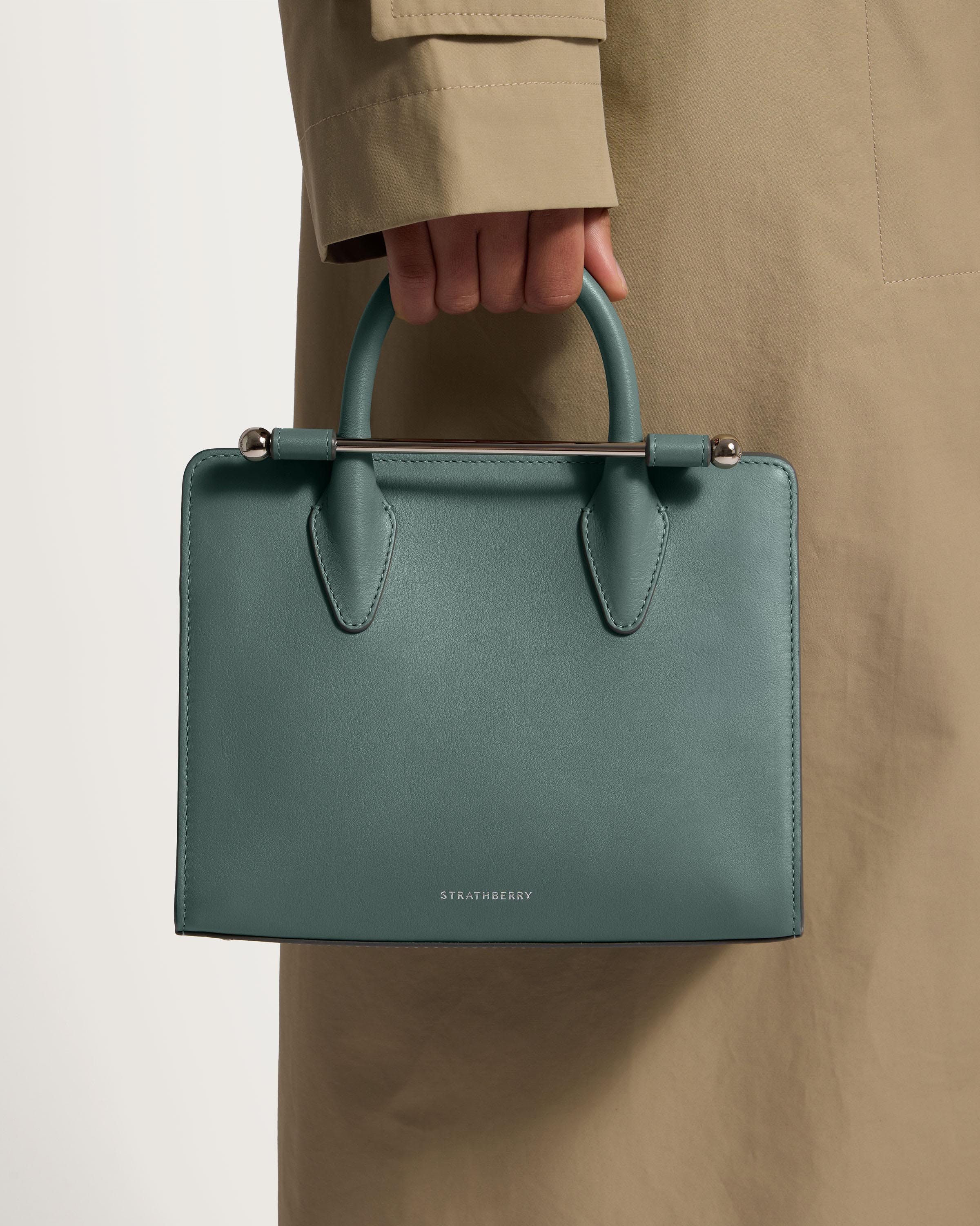 A person in a trench coat holding a green handbag