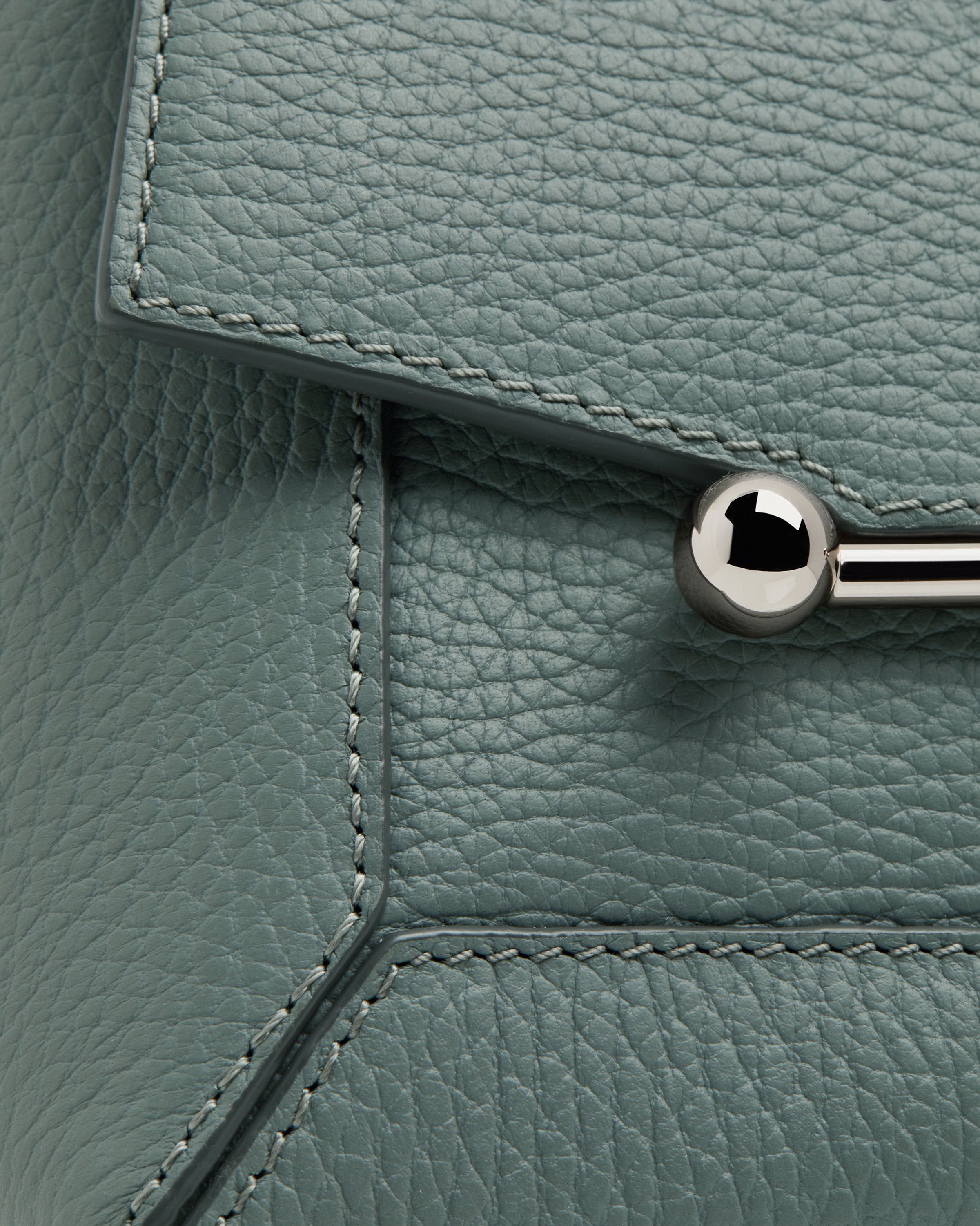 A close up of a metal handle on a green leather bag