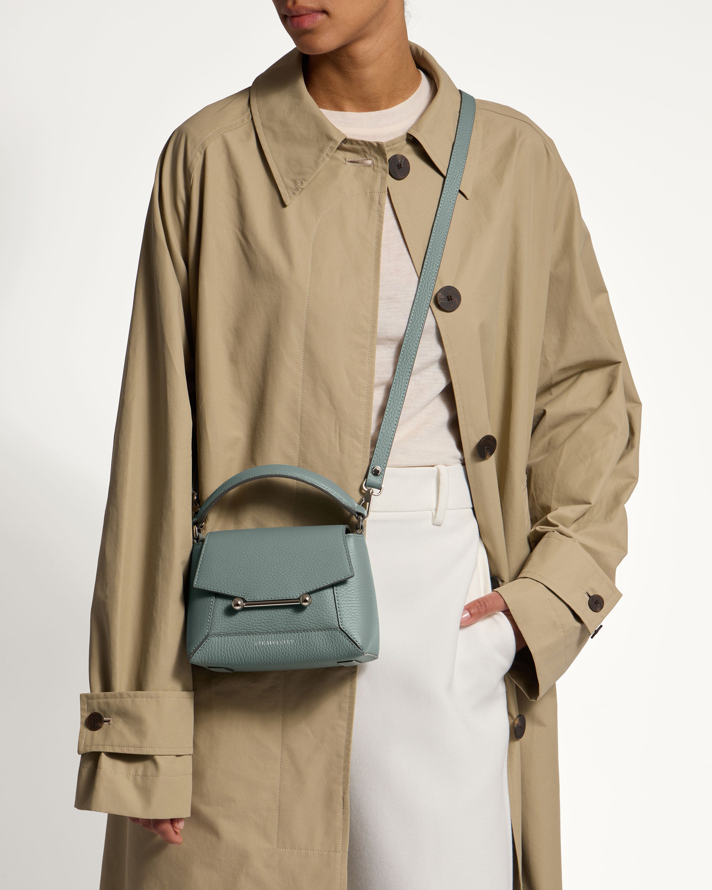 A woman in a trench coat holding a small purse