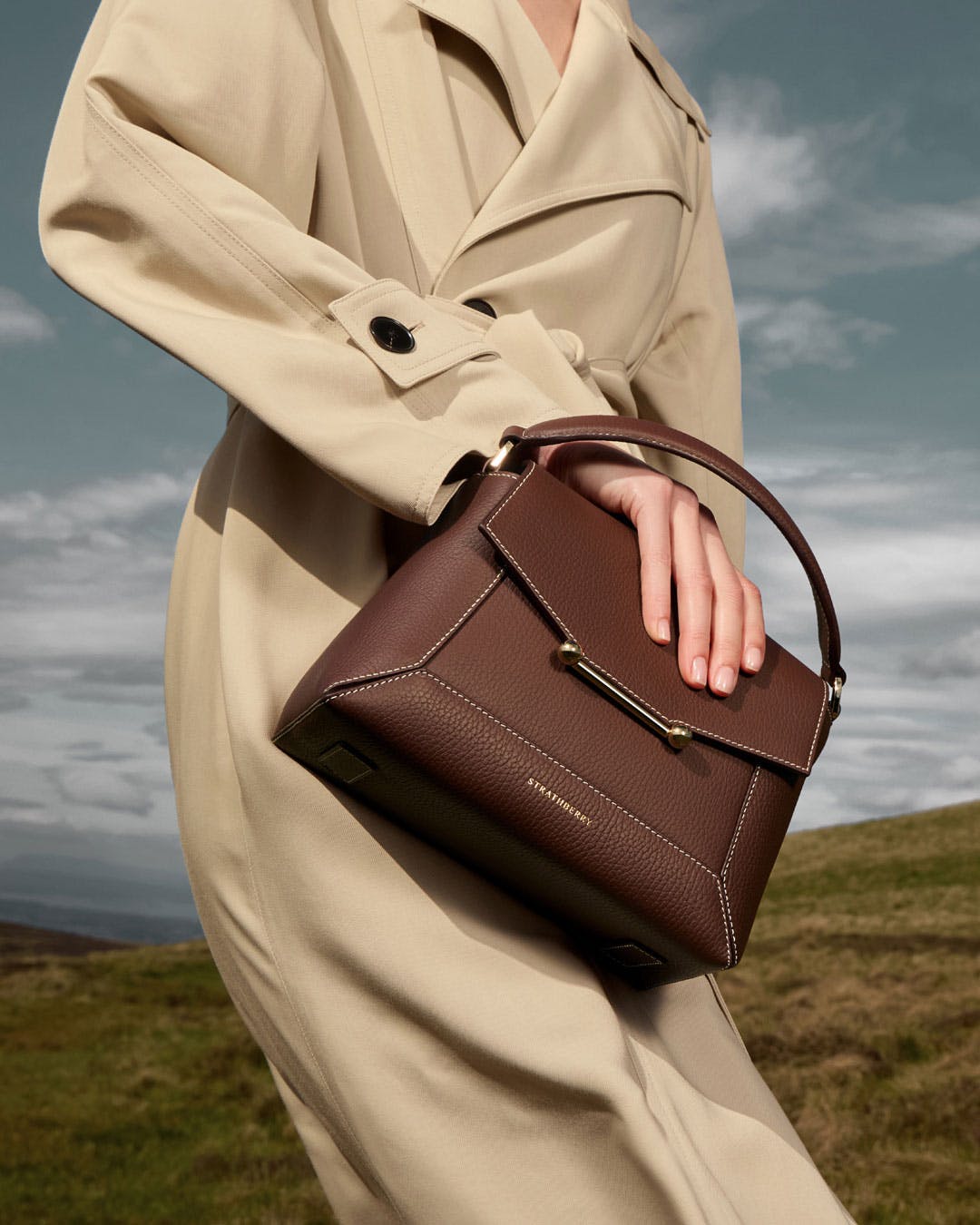 A woman in a trench coat carrying a brown purse