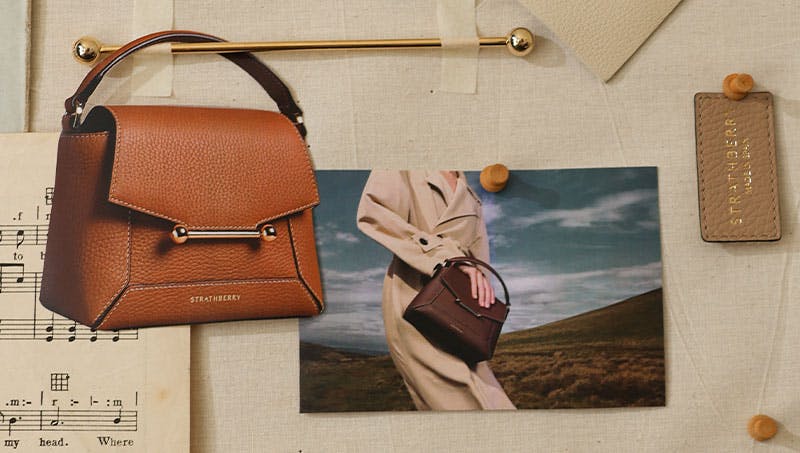 A brown purse sitting on top of a table next to a sheet of paper