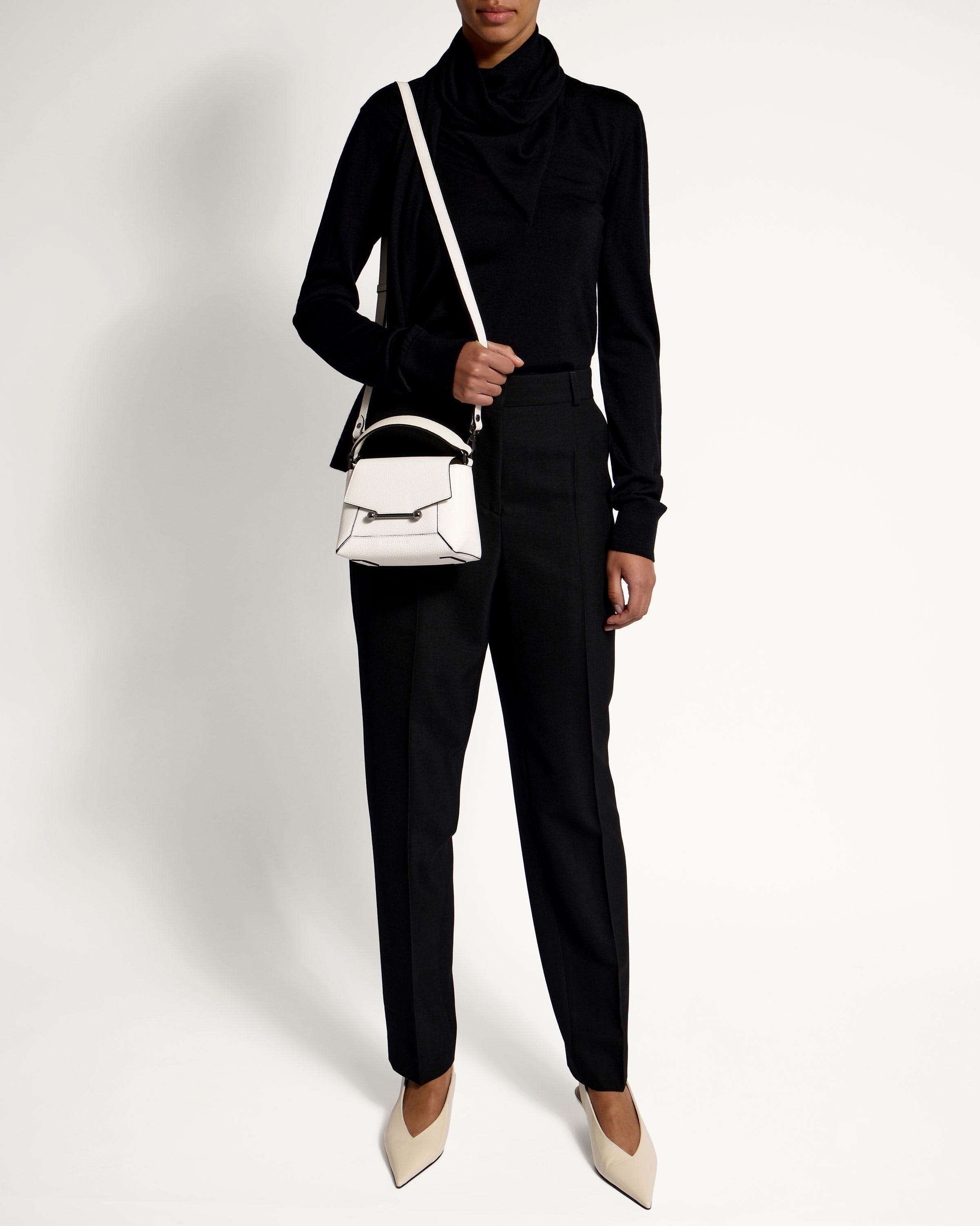 A woman in a black turtle neck sweater holding a white handbag