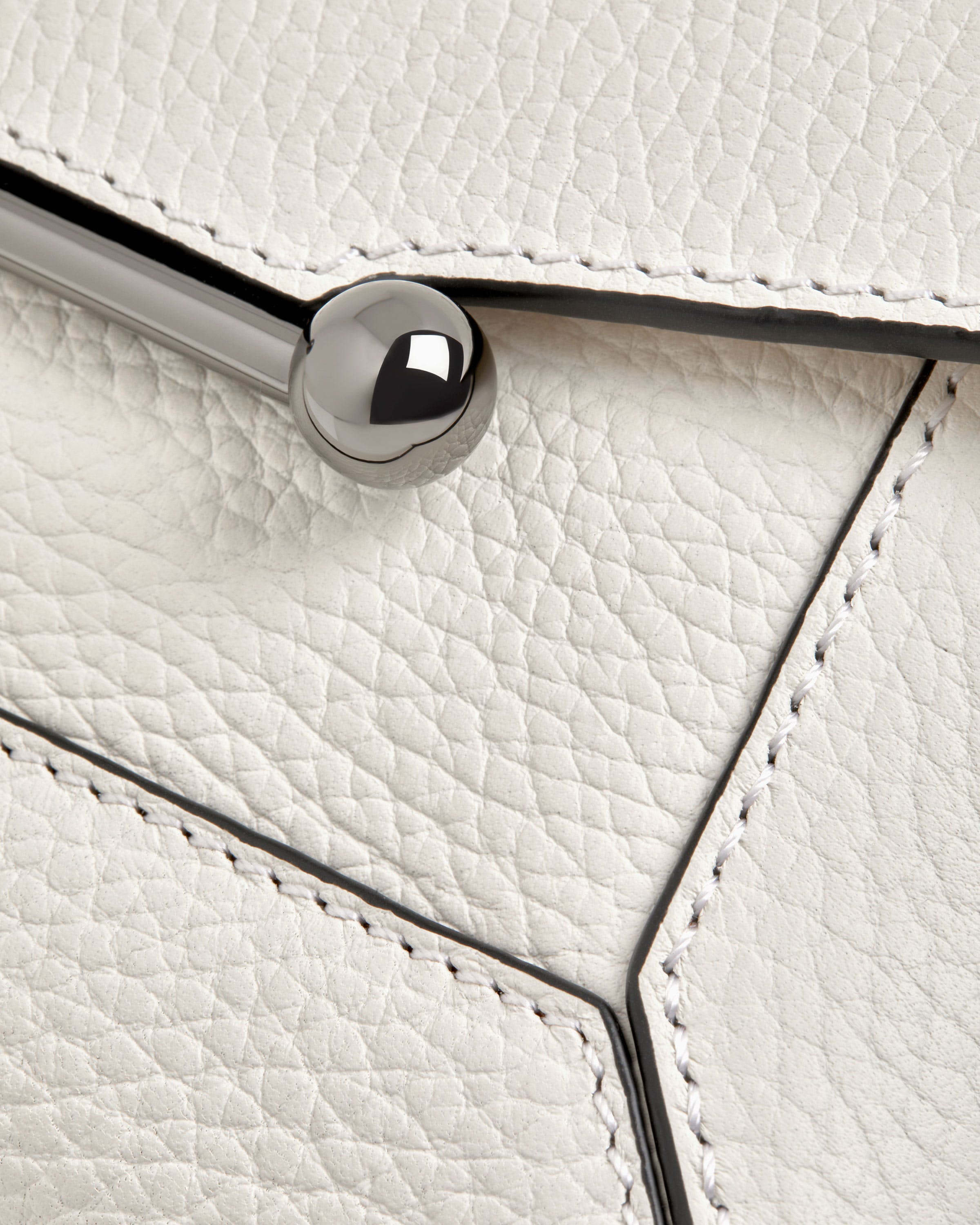 A close up of a white purse with a metal handle