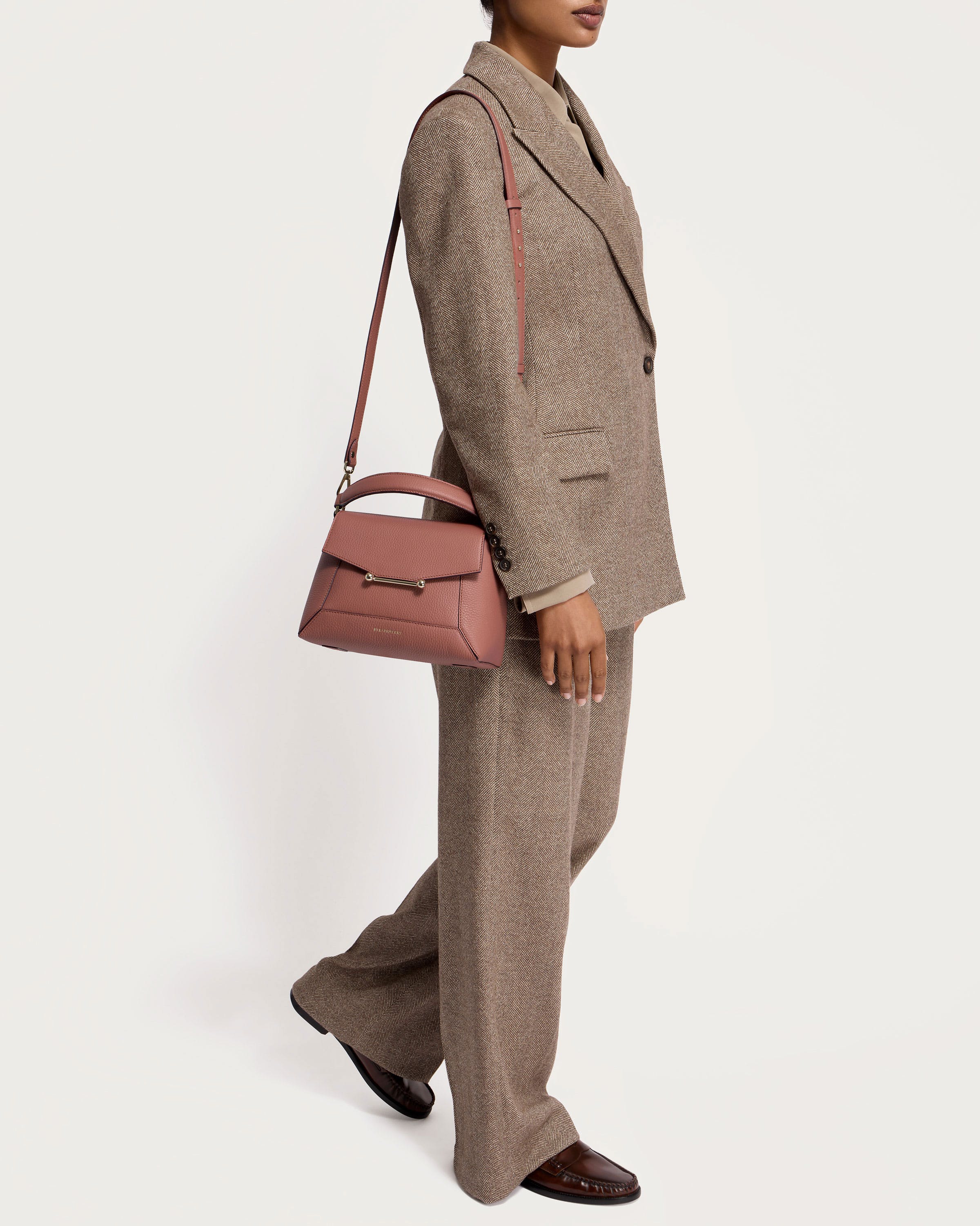 A woman in a suit and hat carrying a pink purse