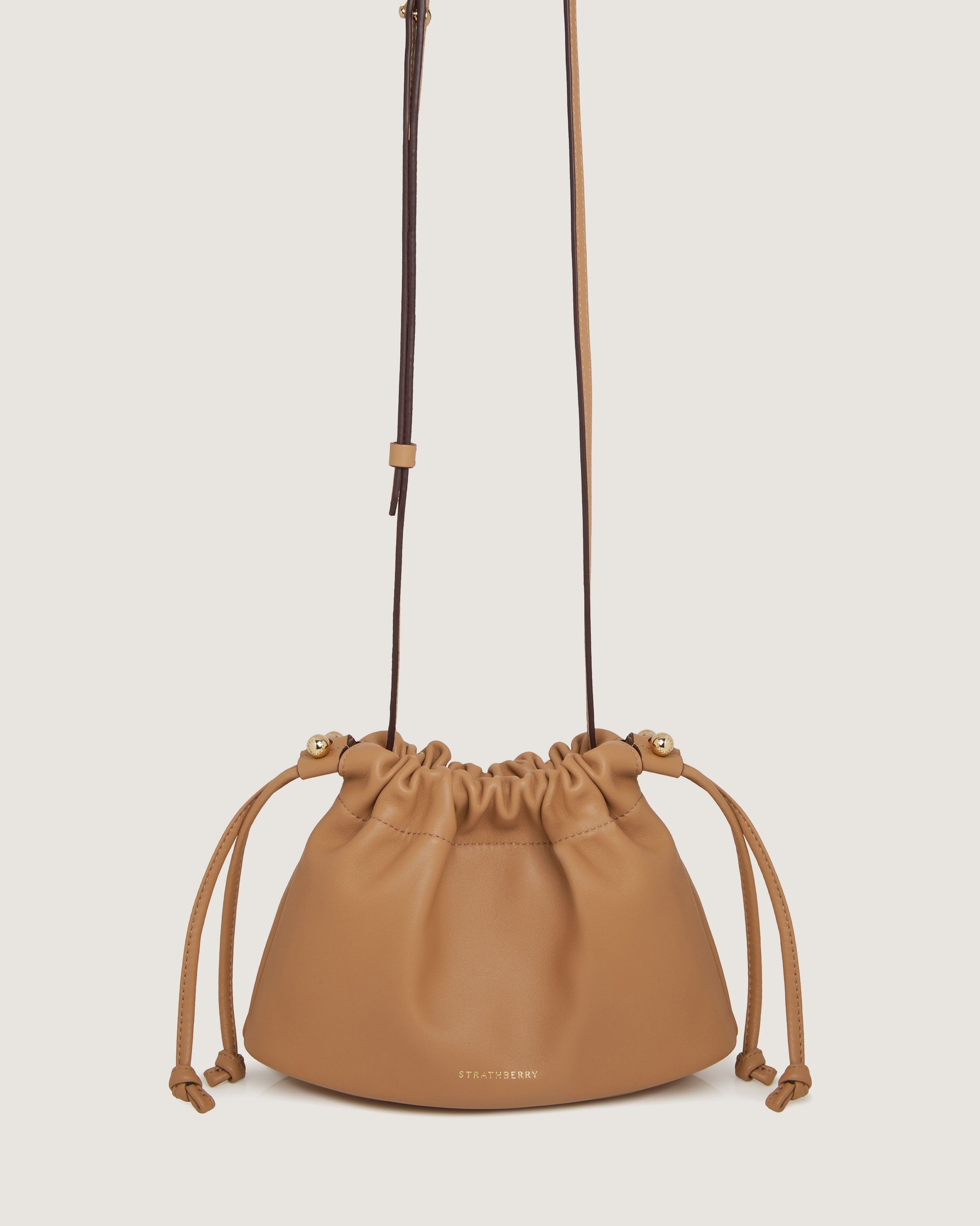 A tan leather bucket bag with a drawstring strap