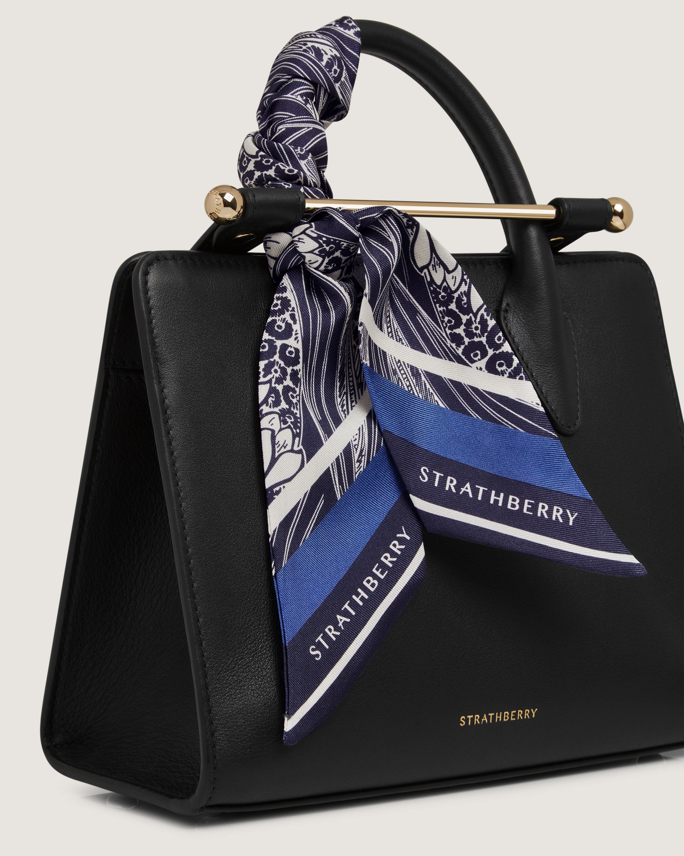 A black handbag with a blue and white scarf tied around it