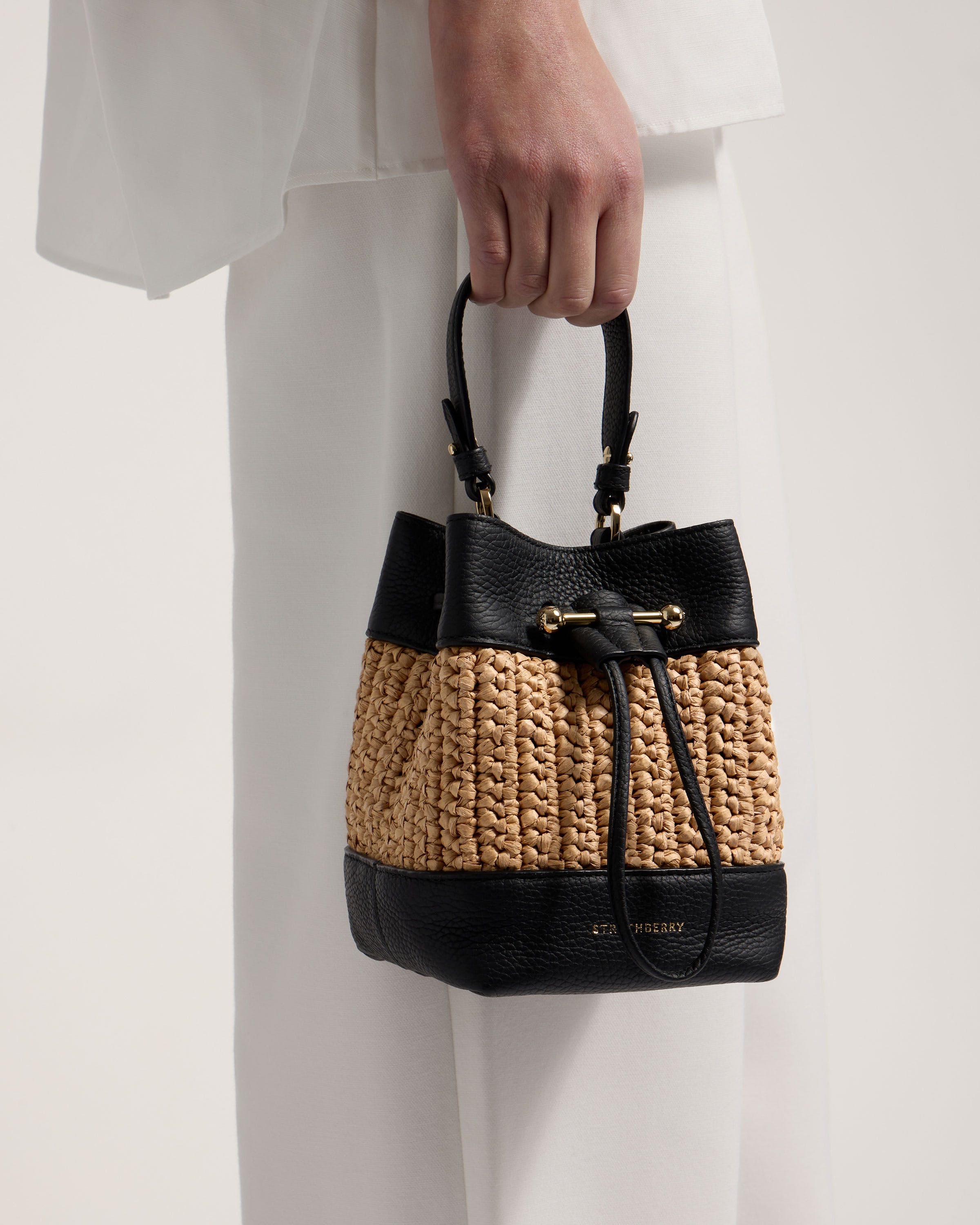 A woman holding a black and tan straw bag