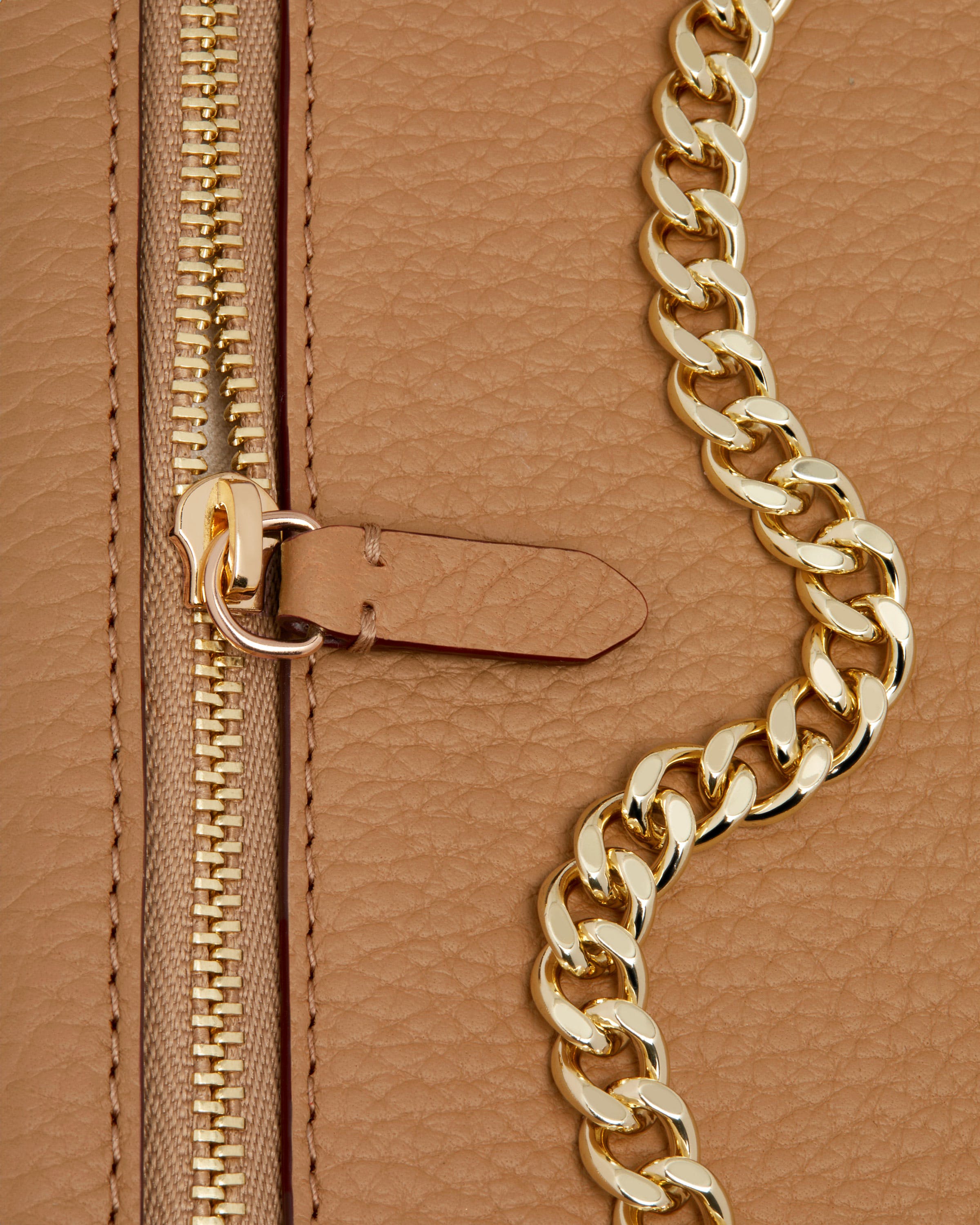 A close up of a gold chain on a tan purse