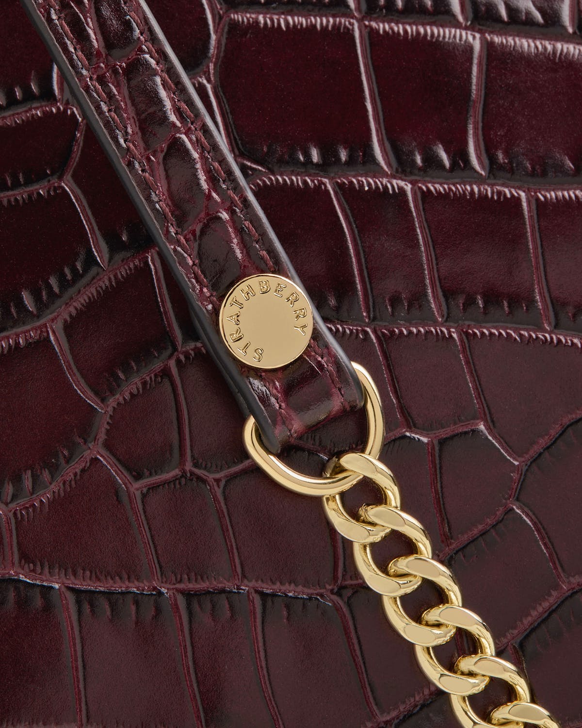 Strathberry croc-effect bag close-up showing strap, gold chain and logo rivet