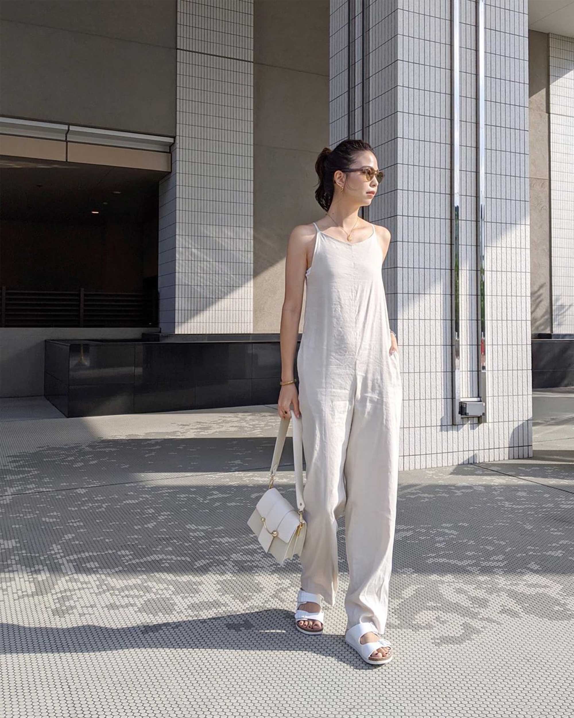 A woman in a white jumpsuit standing in front of a building