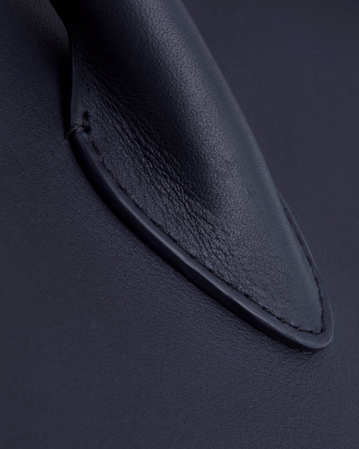 Close-up of marine blue leather midi tote handle and stitched attachment.