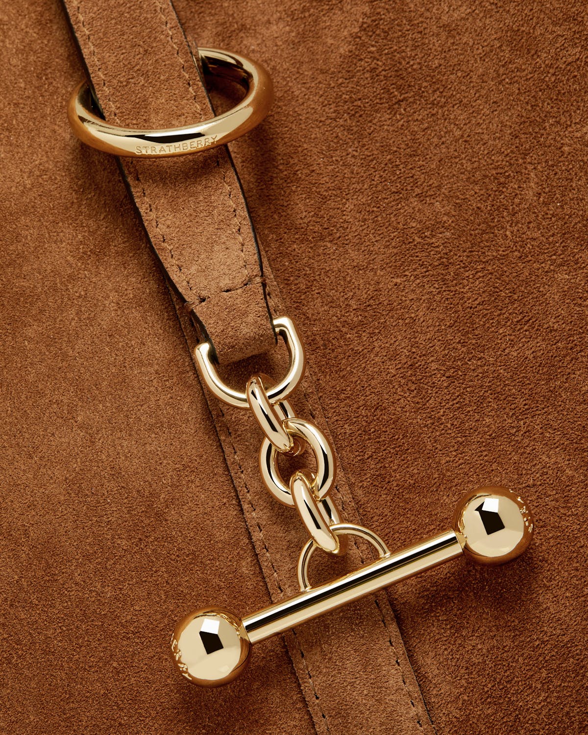 Tan suede bag detail showing Strathberry engraved gold ring and bar toggle.