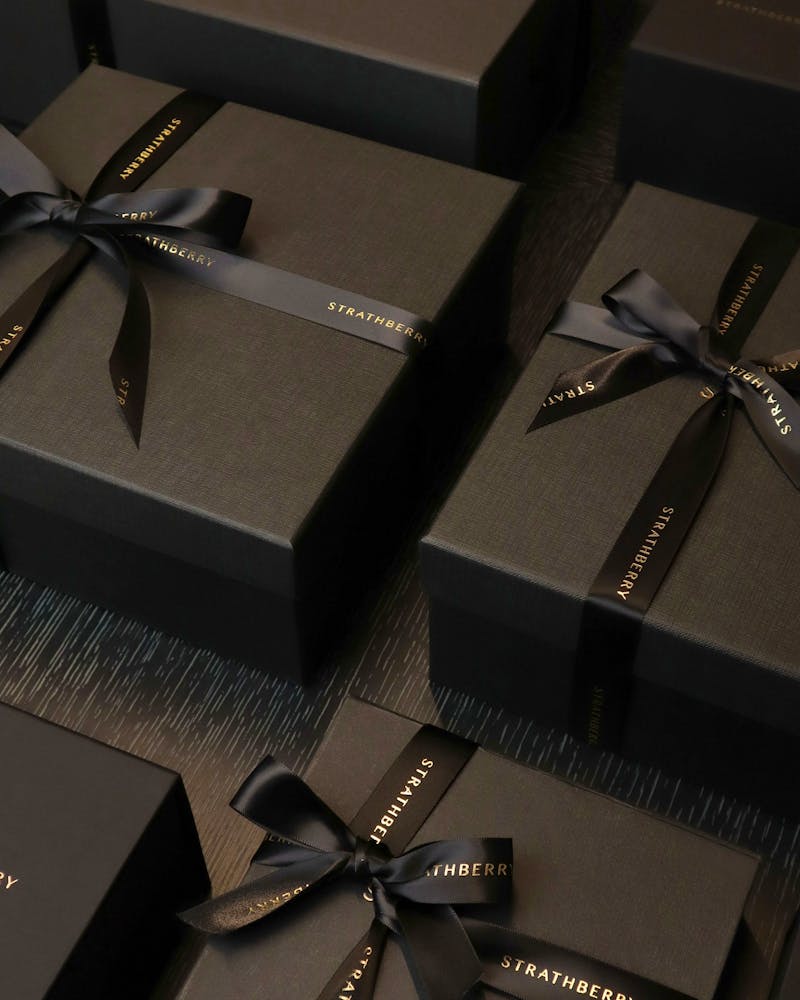 Several black gift boxes tied with black Strathberry ribbons on dark wood
