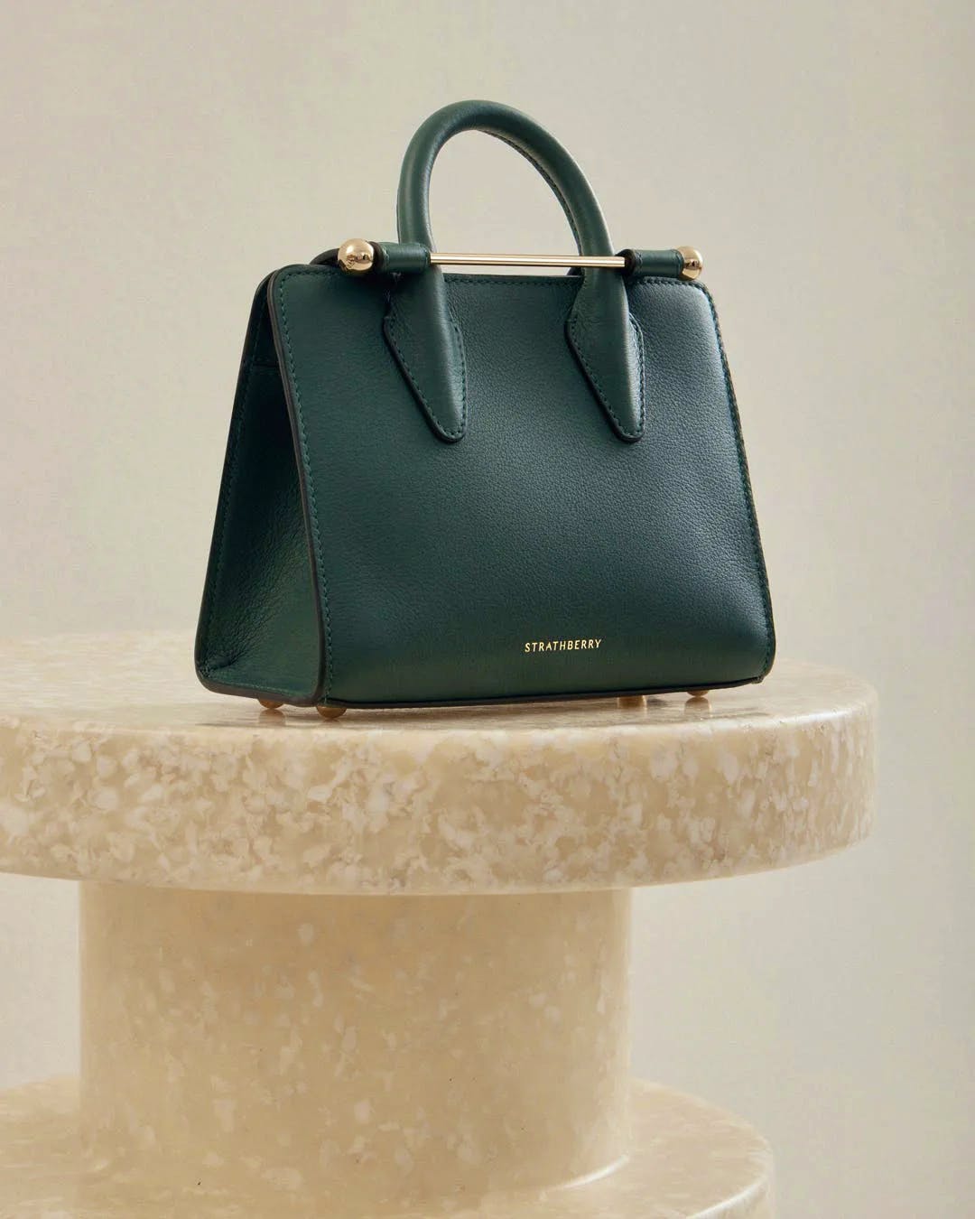Bottle green Strathberry nano tote on a marble pedestal, front view.