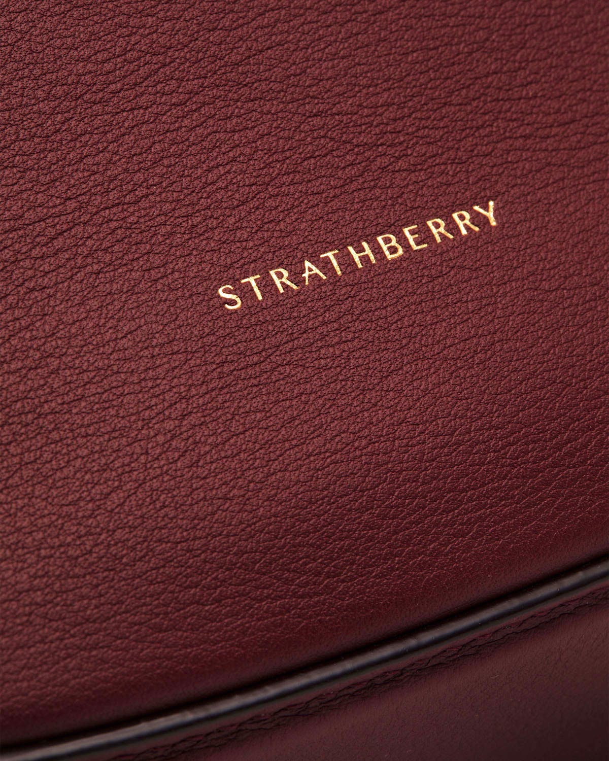 Strathberry logo stamped on oxblood leather crescent moon bag surface.