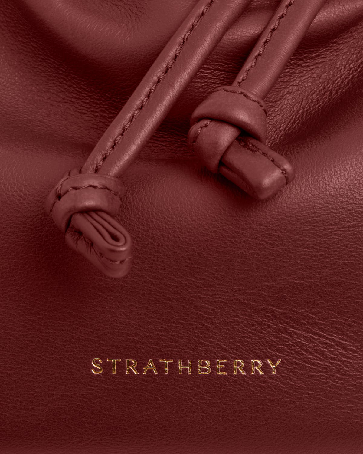 Oxblood leather with stitched knotted drawstrings, textured grain and gold Strathberry logo