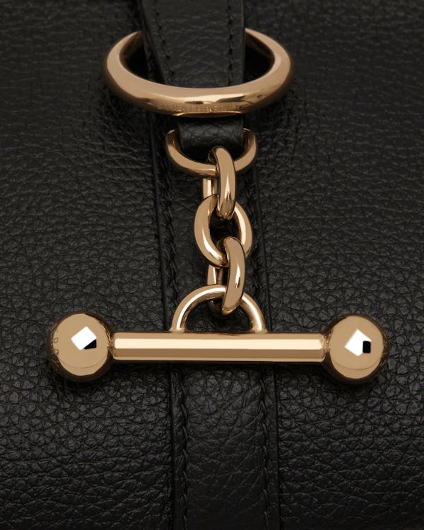 Close-up of Strathberry black pebbled leather with gold chain and bar closure.