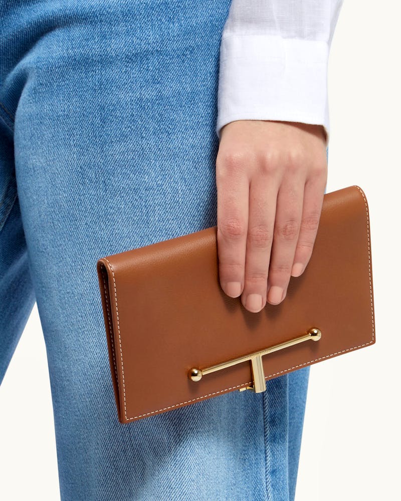 Hand holding chestnut large Melville Street wallet with vanilla stitching and gold bar.