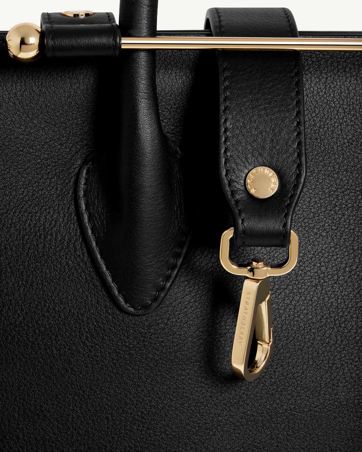 Close-up front of Strathberry black midi tote showing gold hardware and strap.