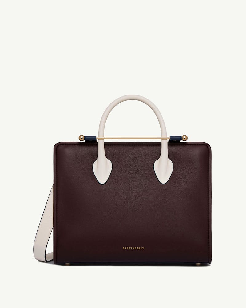 Strathberry midi tote in burgundy with vanilla handles, navy trim, and gold bar.