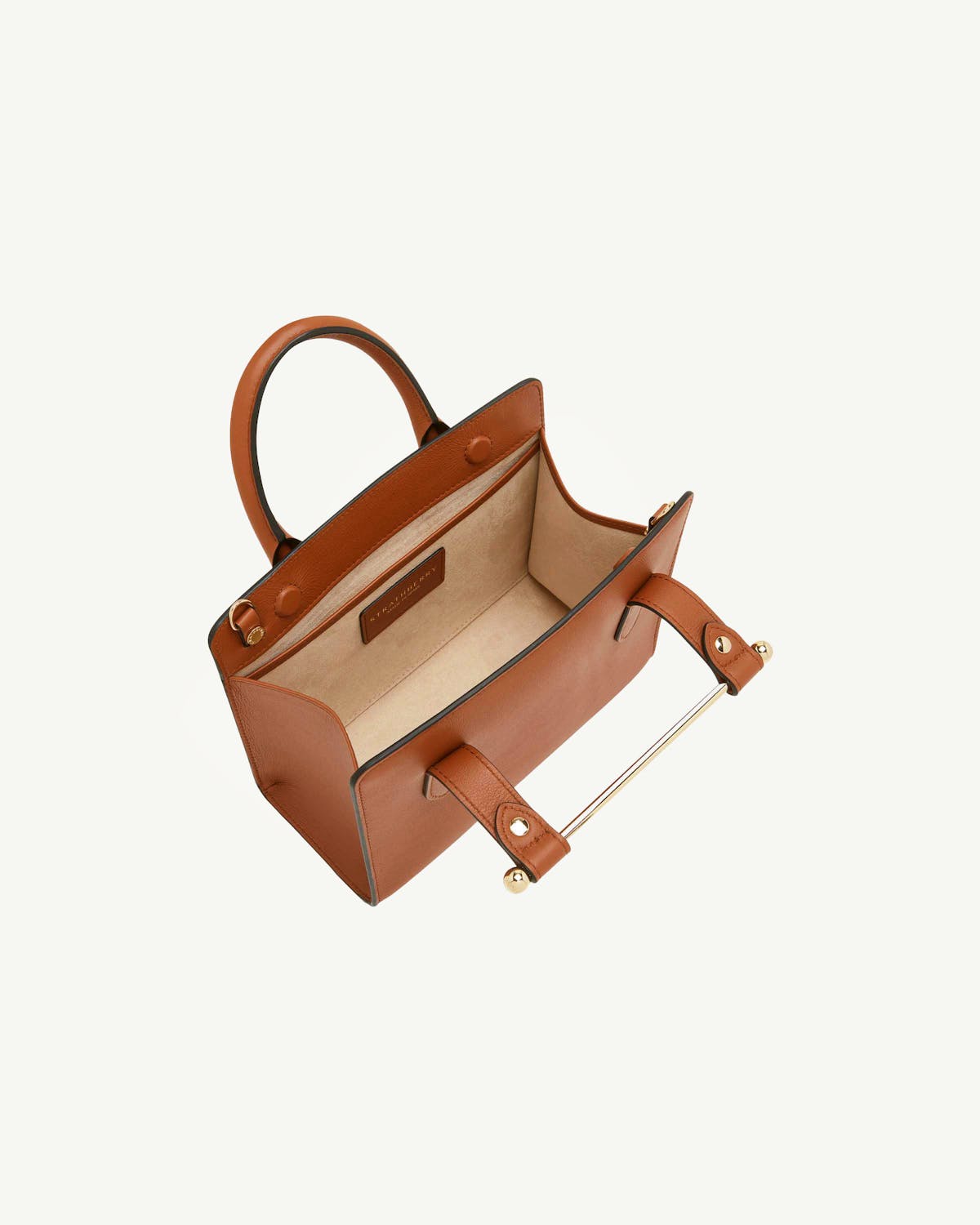 Chestnut Strathberry mini tote on table, open top with visible gold bar handle