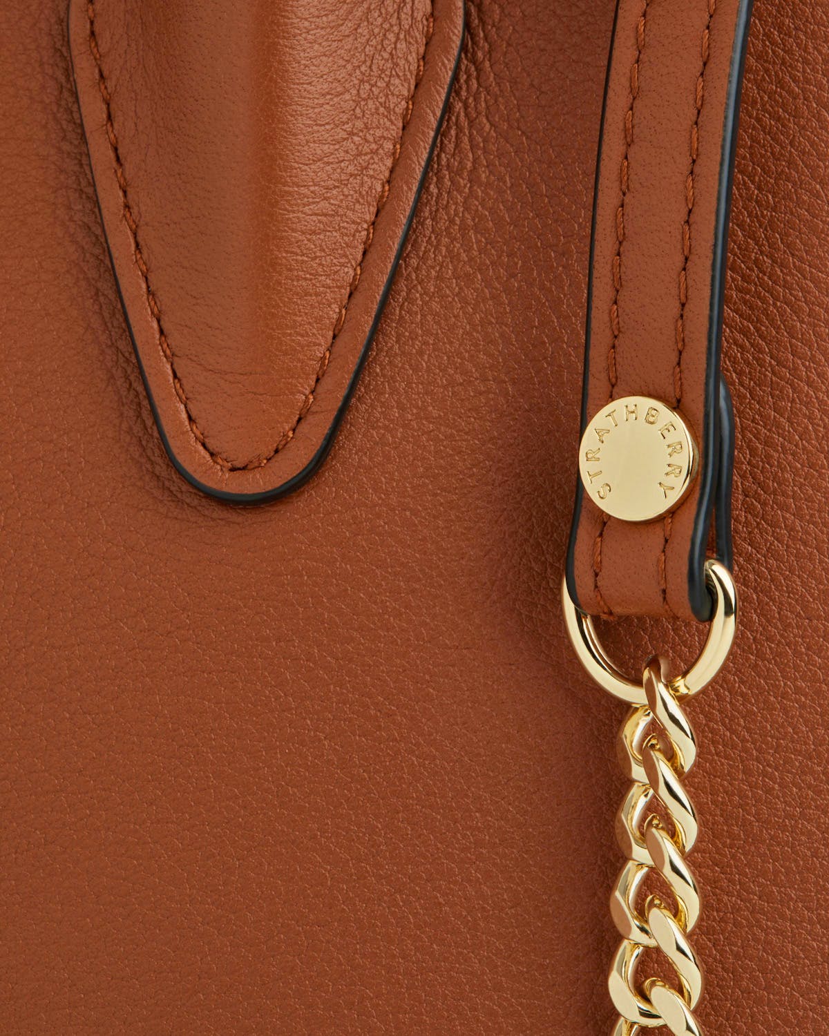 Chestnut Strathberry mini tote close-up showing leather, stitched handle tab, and gold chain.