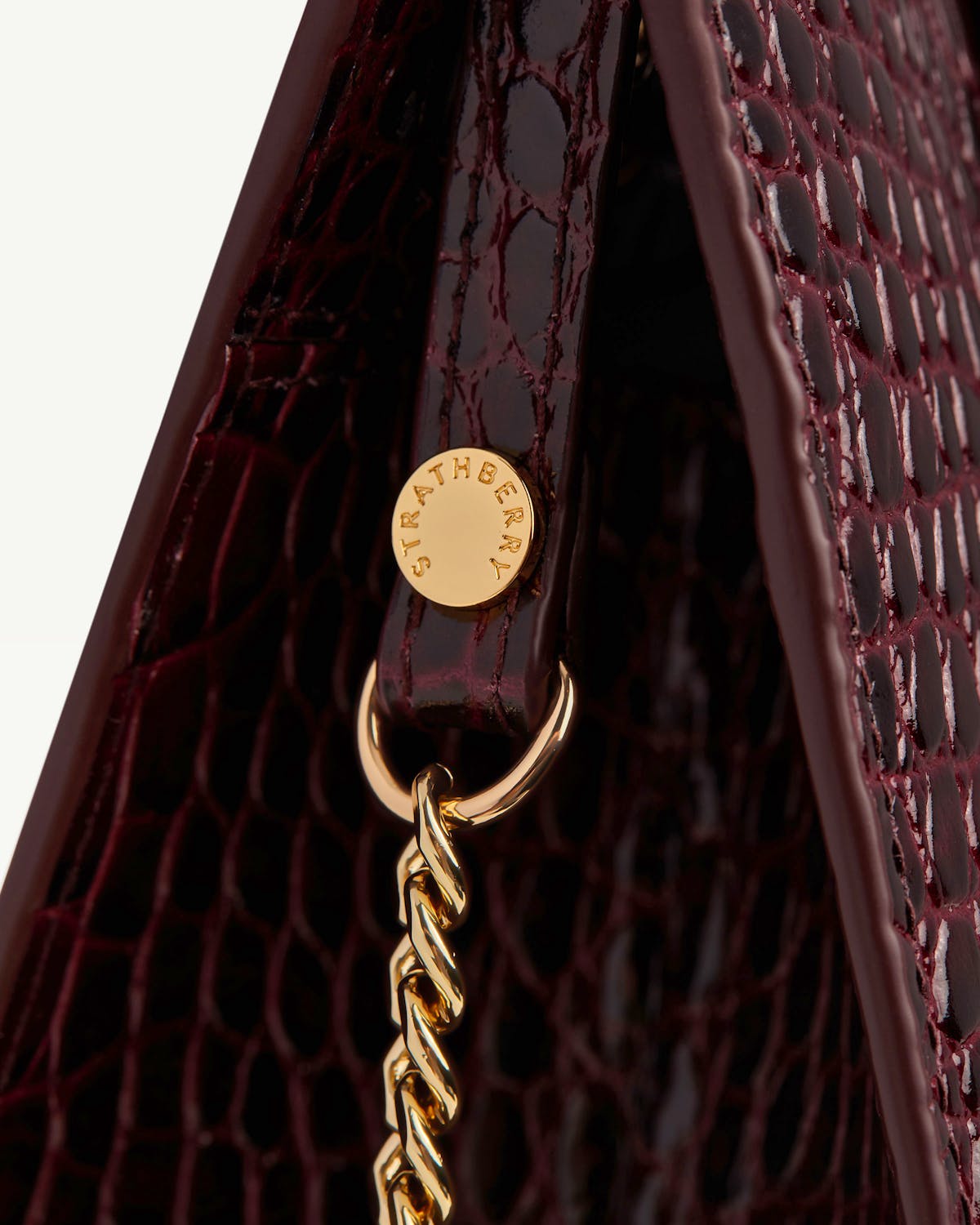 Strathberry croc-effect mini tote side close-up showing gold chain and stud