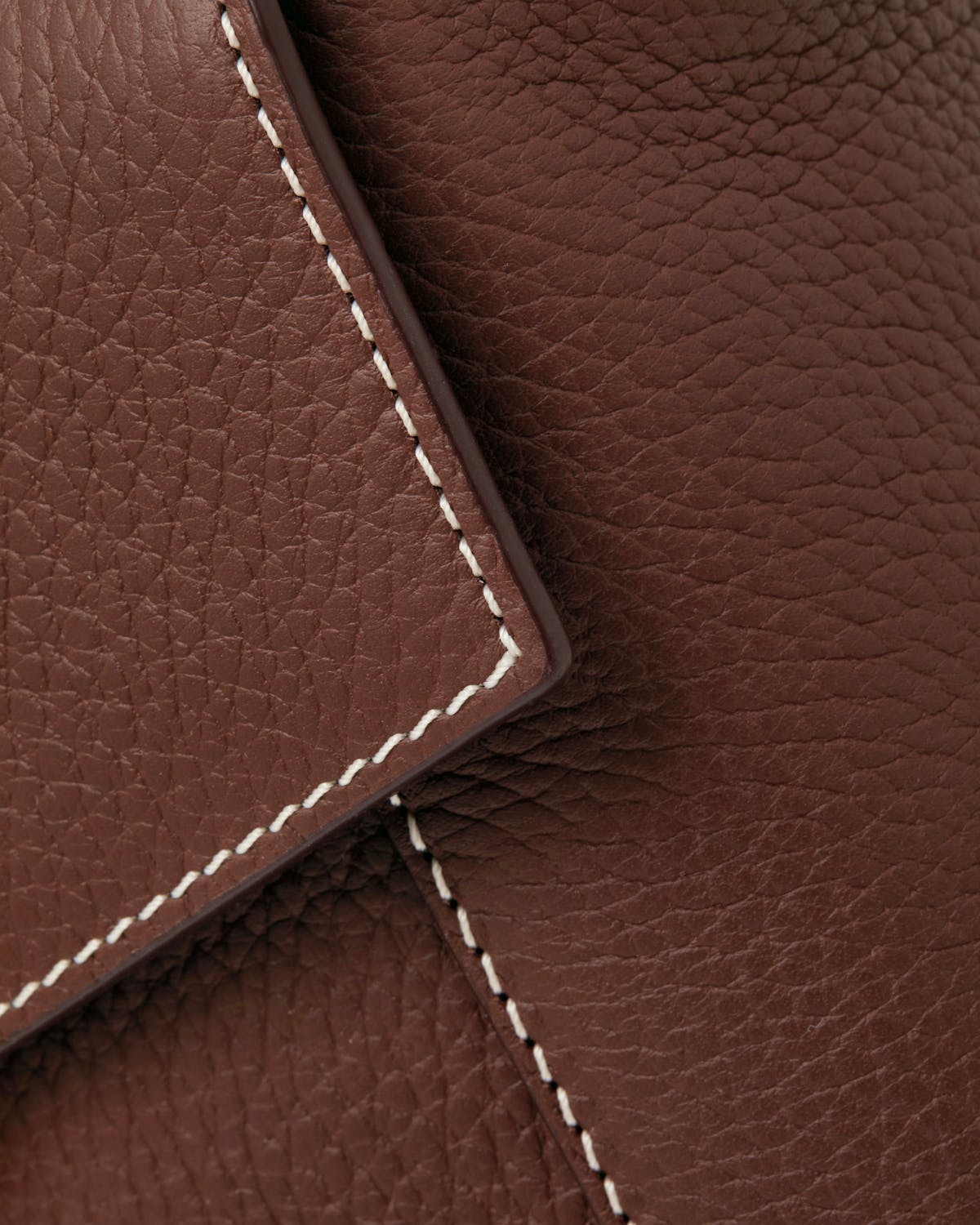 Close-up of chocolate leather bag flap with vanilla contrast stitching