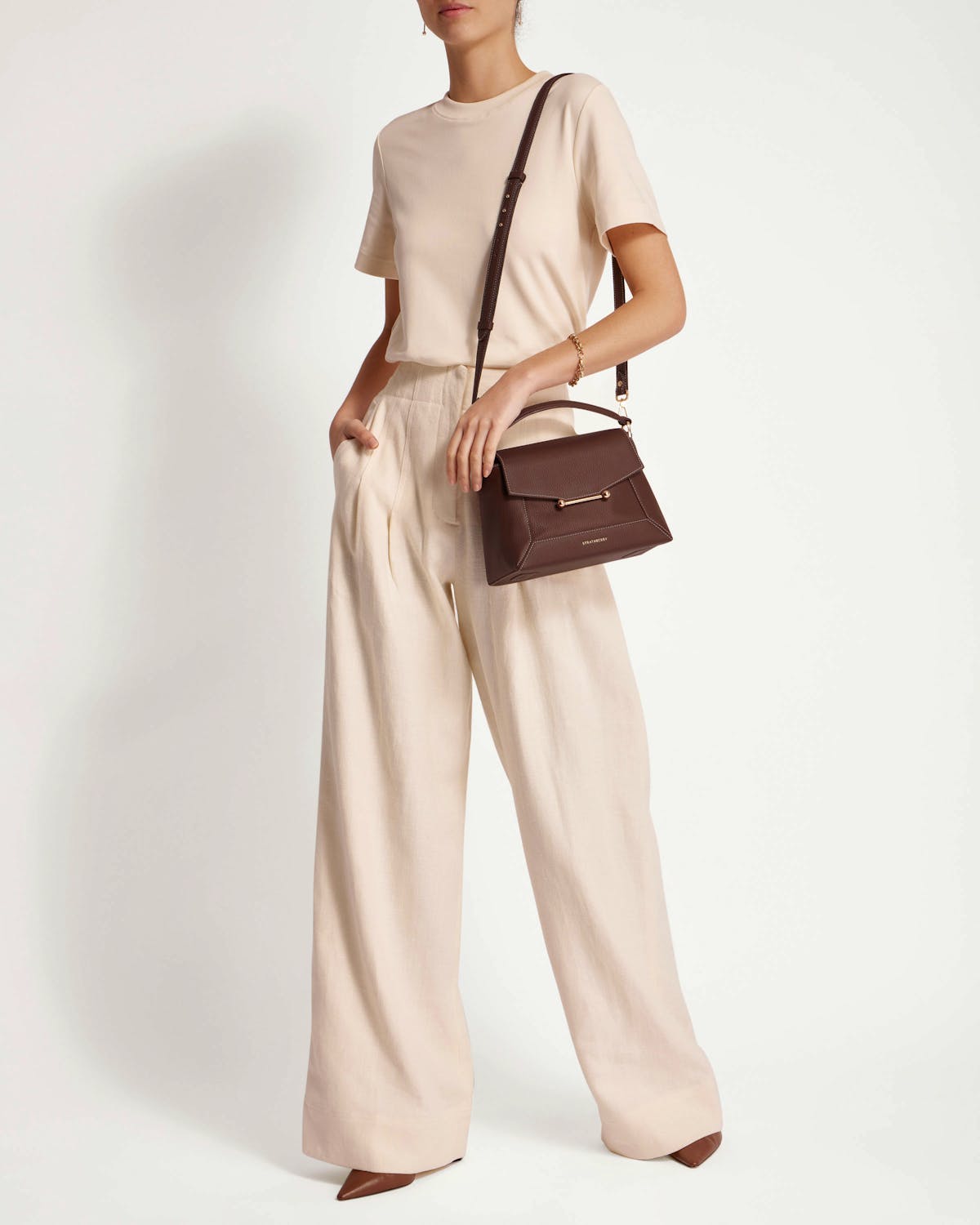 Model standing wearing chocolate mosaic bag crossbody and holding the top handle.